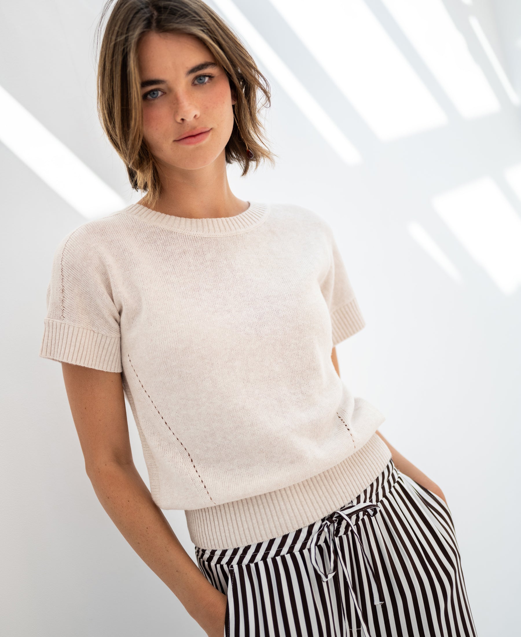 Woman wearing a PLEIN PUBLIQUE summer sweater with linen in light sand, on a white background.