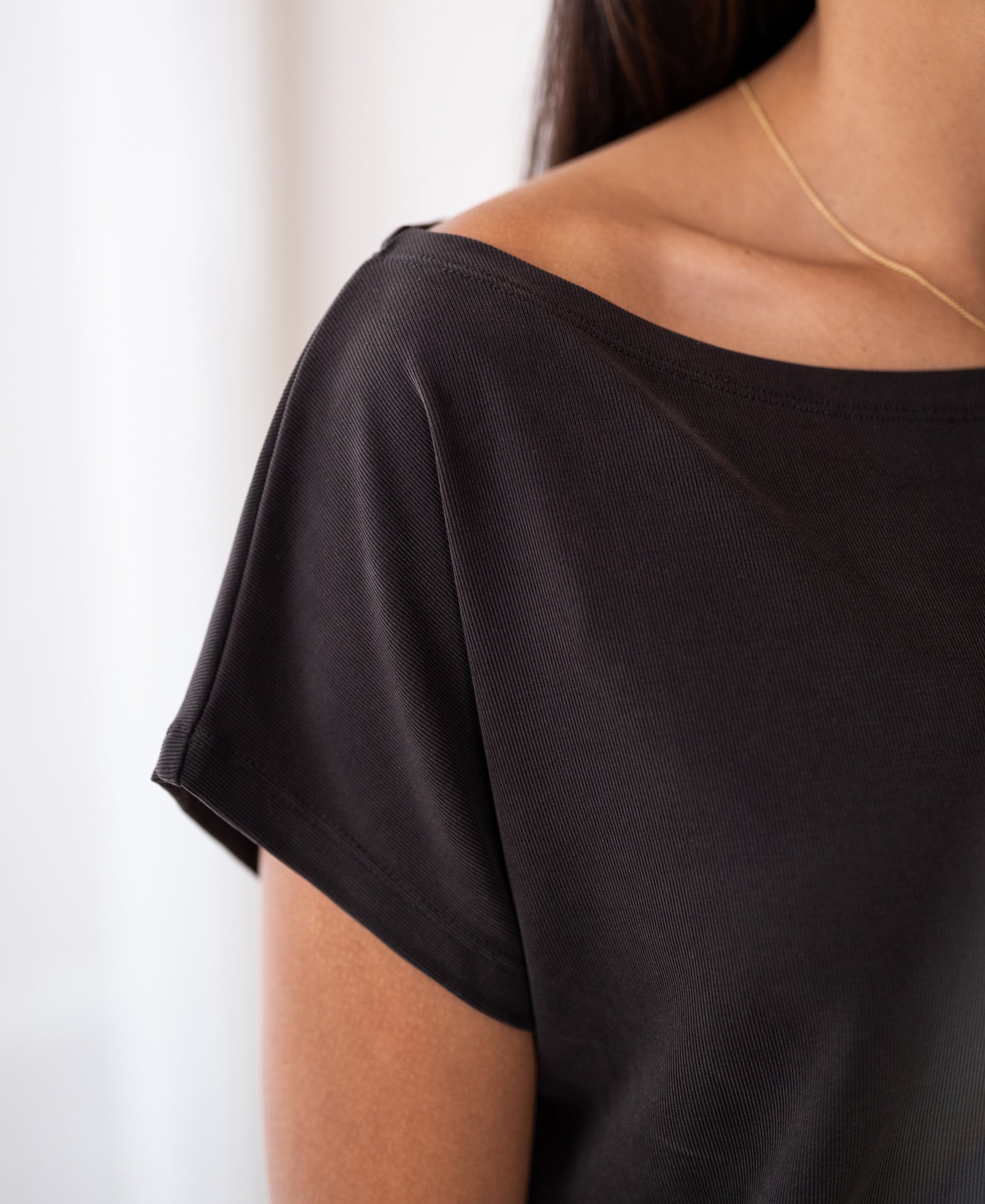 Woman wearing ribbed boat neck T-shirt in pure chocolate brown, shown from shoulders up.