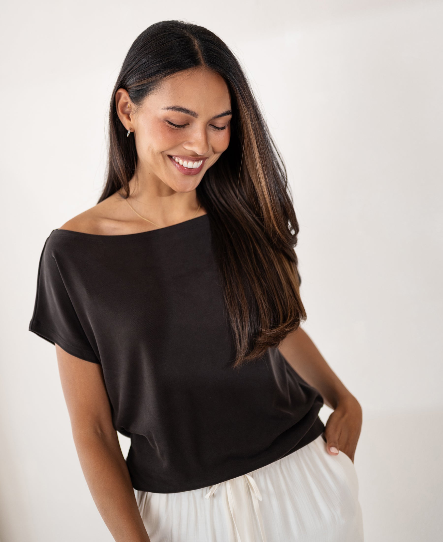Woman wearing a ribbed boat neck T-shirt in pure chocolate brown, smiling and looking down.
