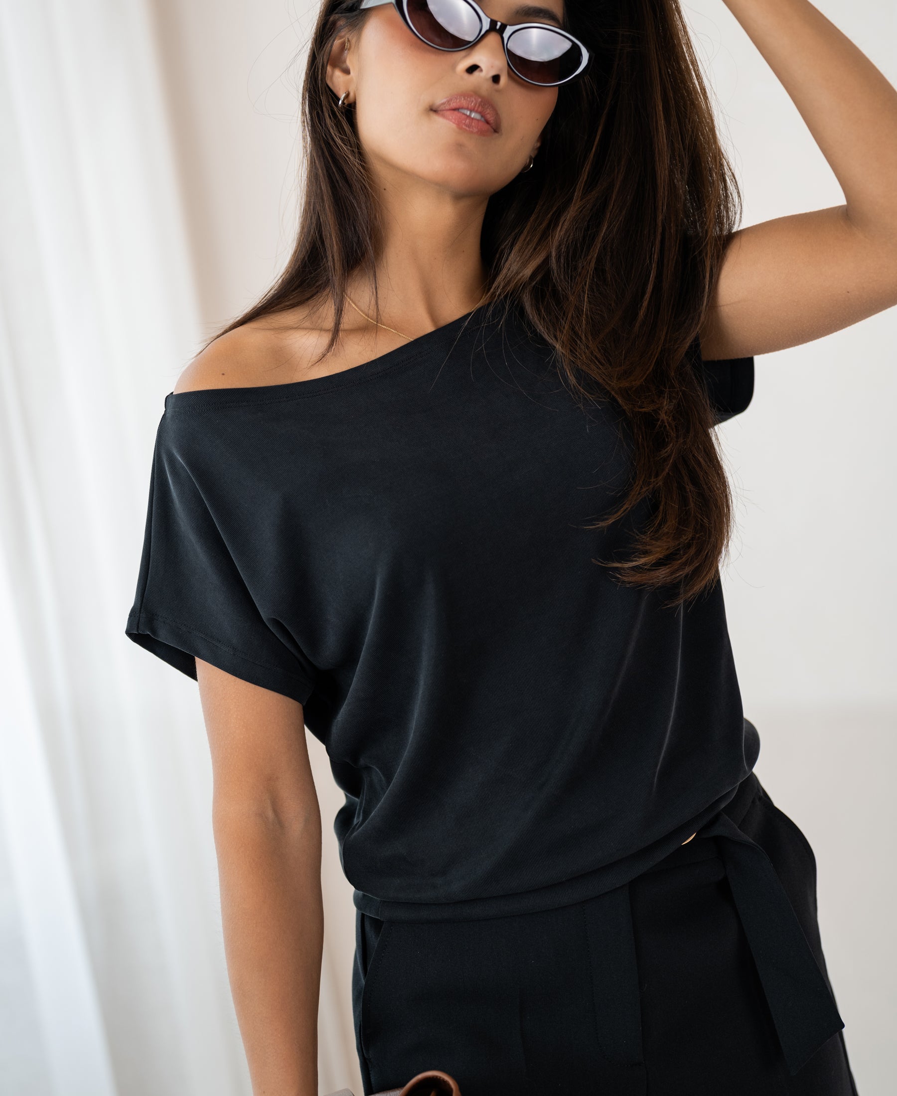 Woman wearing ribbed charcoal boat neck T-shirt stands indoors, looking confidently.
