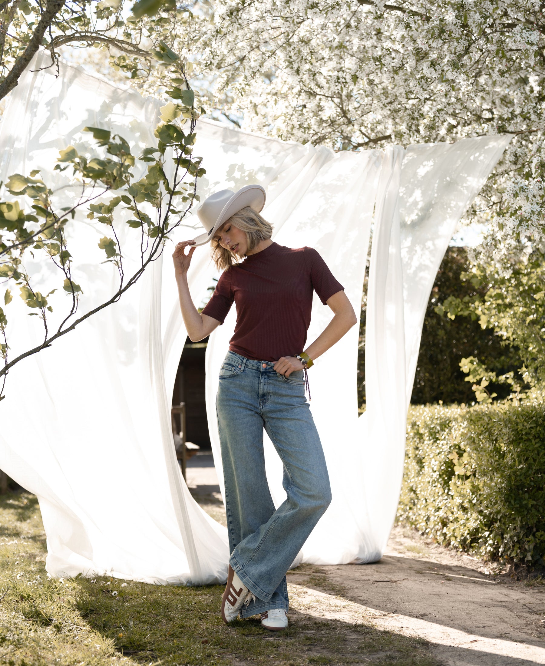Woman wears a bamboo turtleneck top in red-brown by PLEIN PUBLIQUE, shown outdoors on a sunny day.