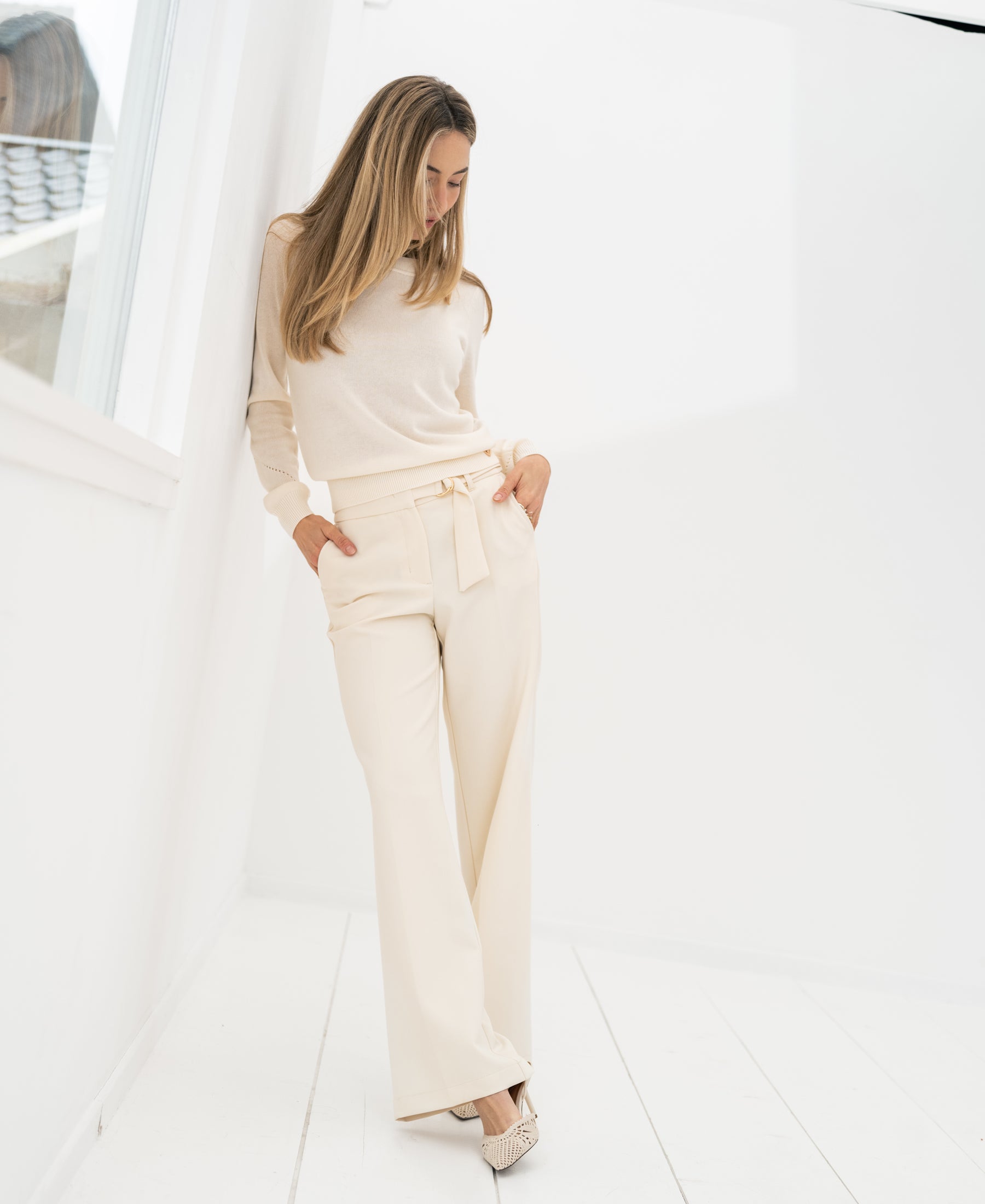 Cream-colored women's pants displayed in a bright, minimalist room against a white wall.