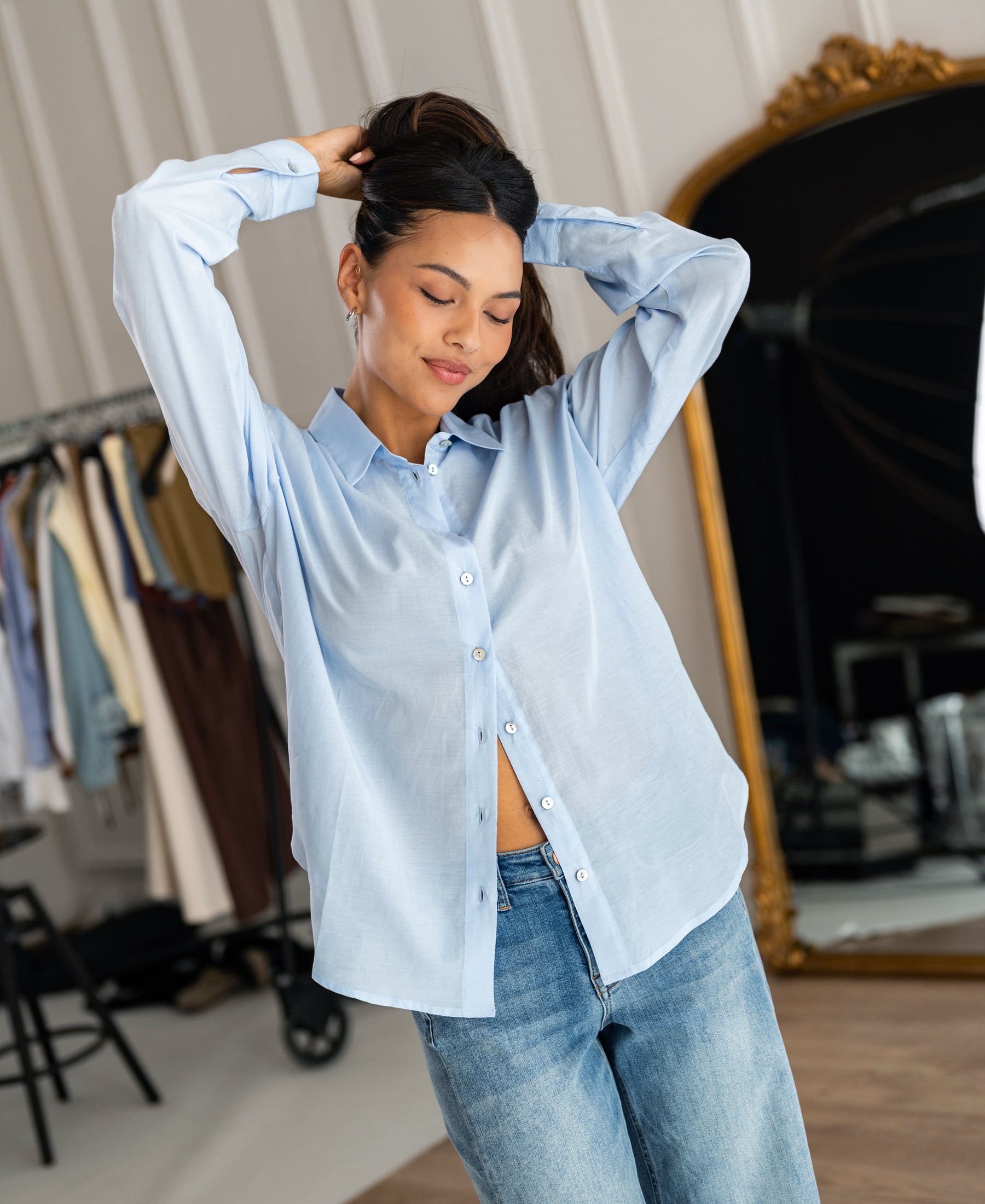 Dunne oversized blouse in light blue silk by PLEIN PUBLIQUE, shown worn in a chic indoor setting.