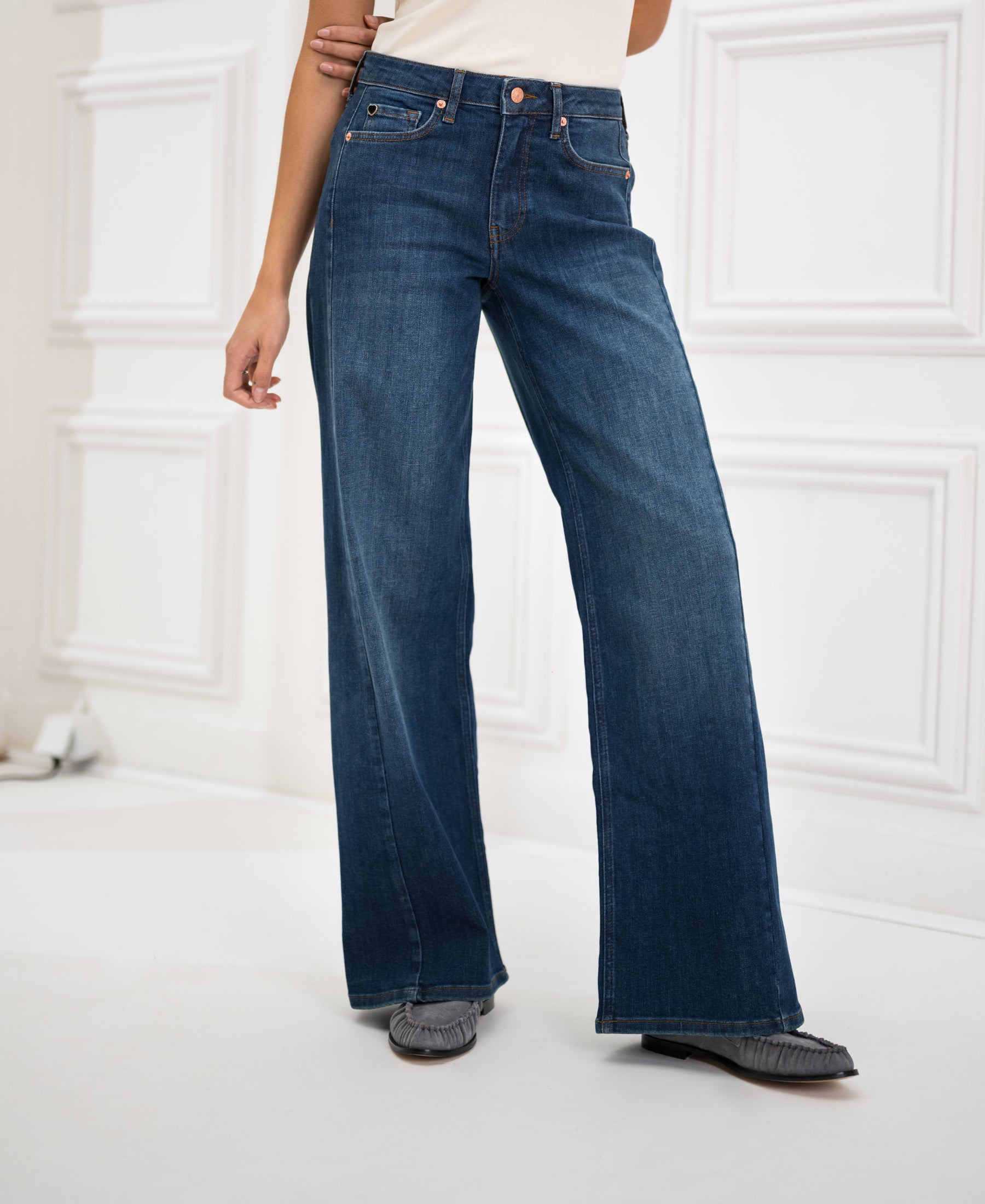 Wide leg jeans in blue heritage wash, shown standing in a white room with paneled walls.