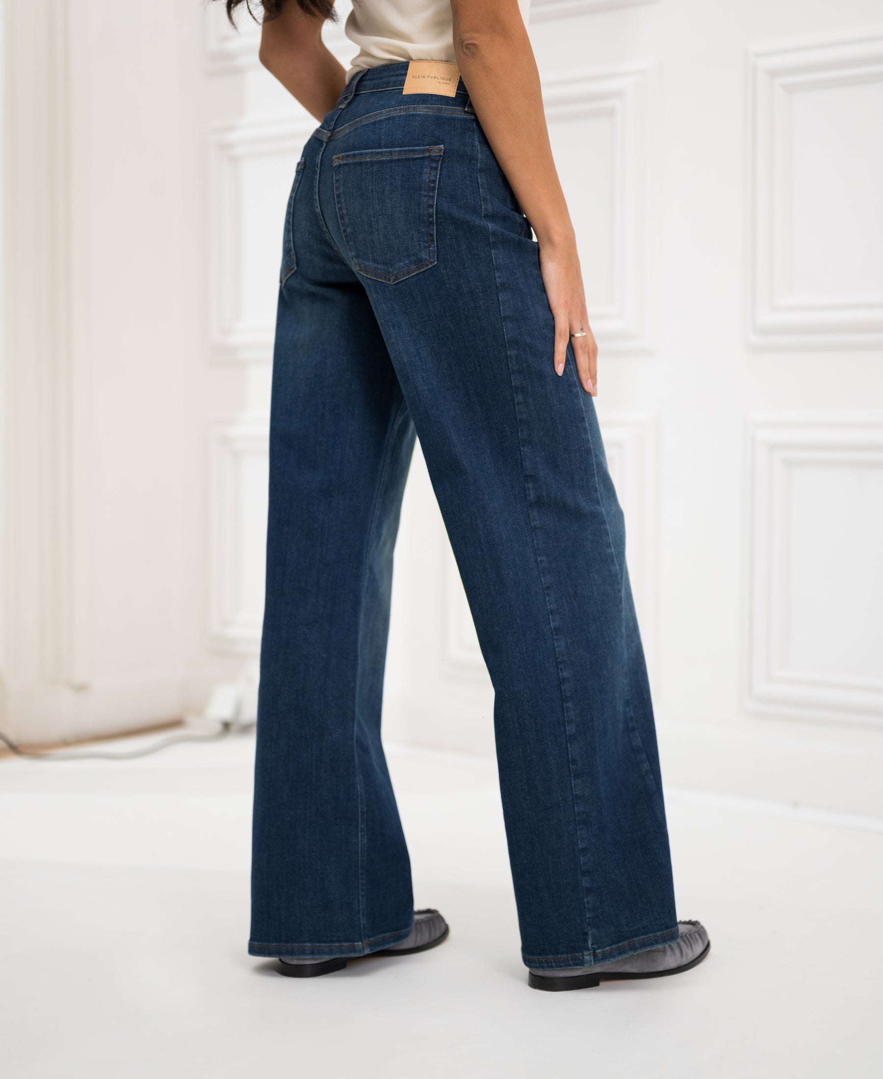 Wide leg jeans in blue heritage color, shown indoors against white paneled walls.