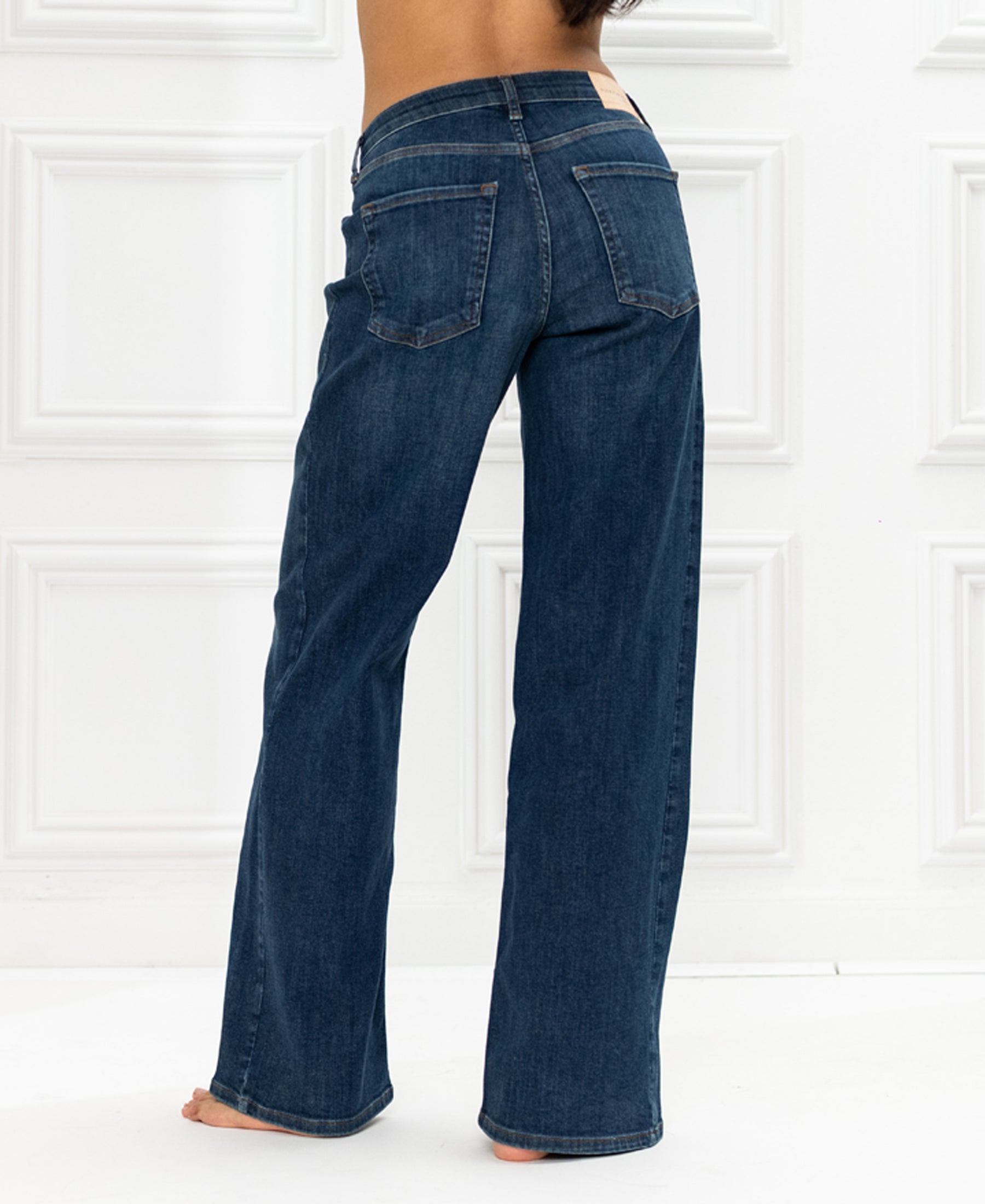 Wide leg blue heritage jeans, back view against a white paneled wall.