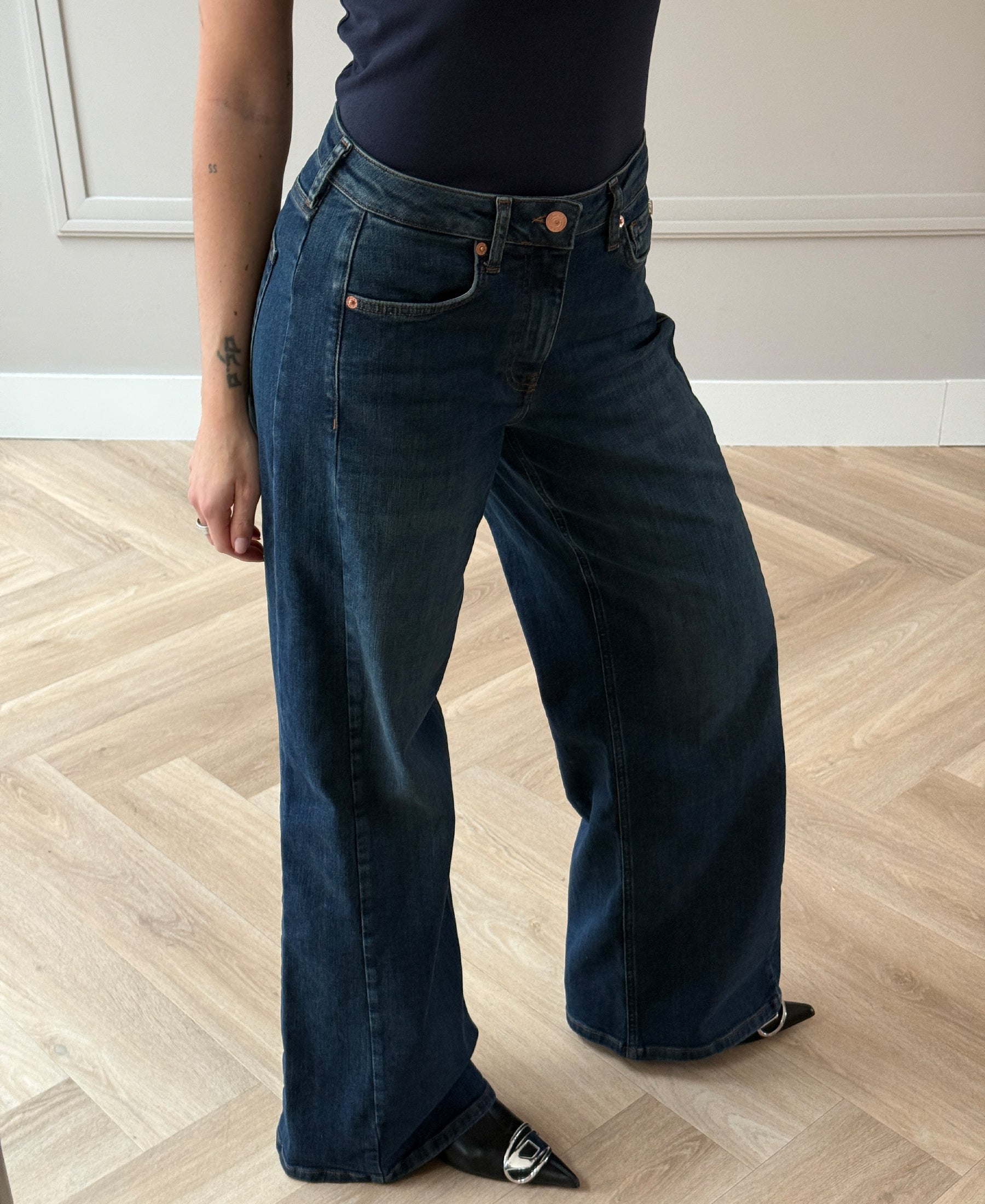 Wide leg jeans in blue made from organic cotton, shown on a light wooden floor.