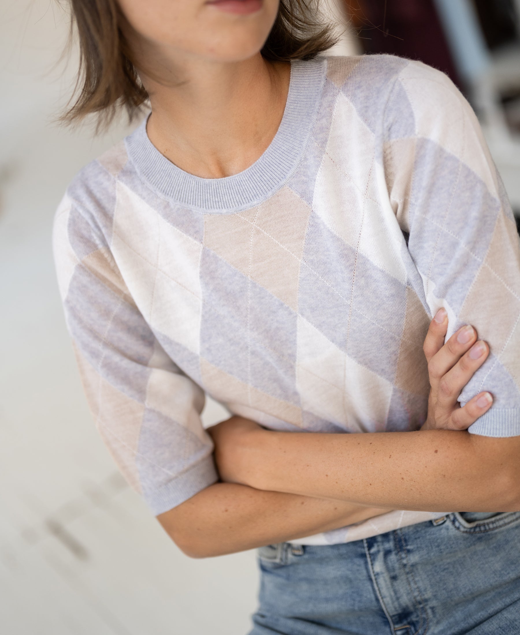 Argyle merino wool sweater in light grey melange, shown with model standing arms crossed.