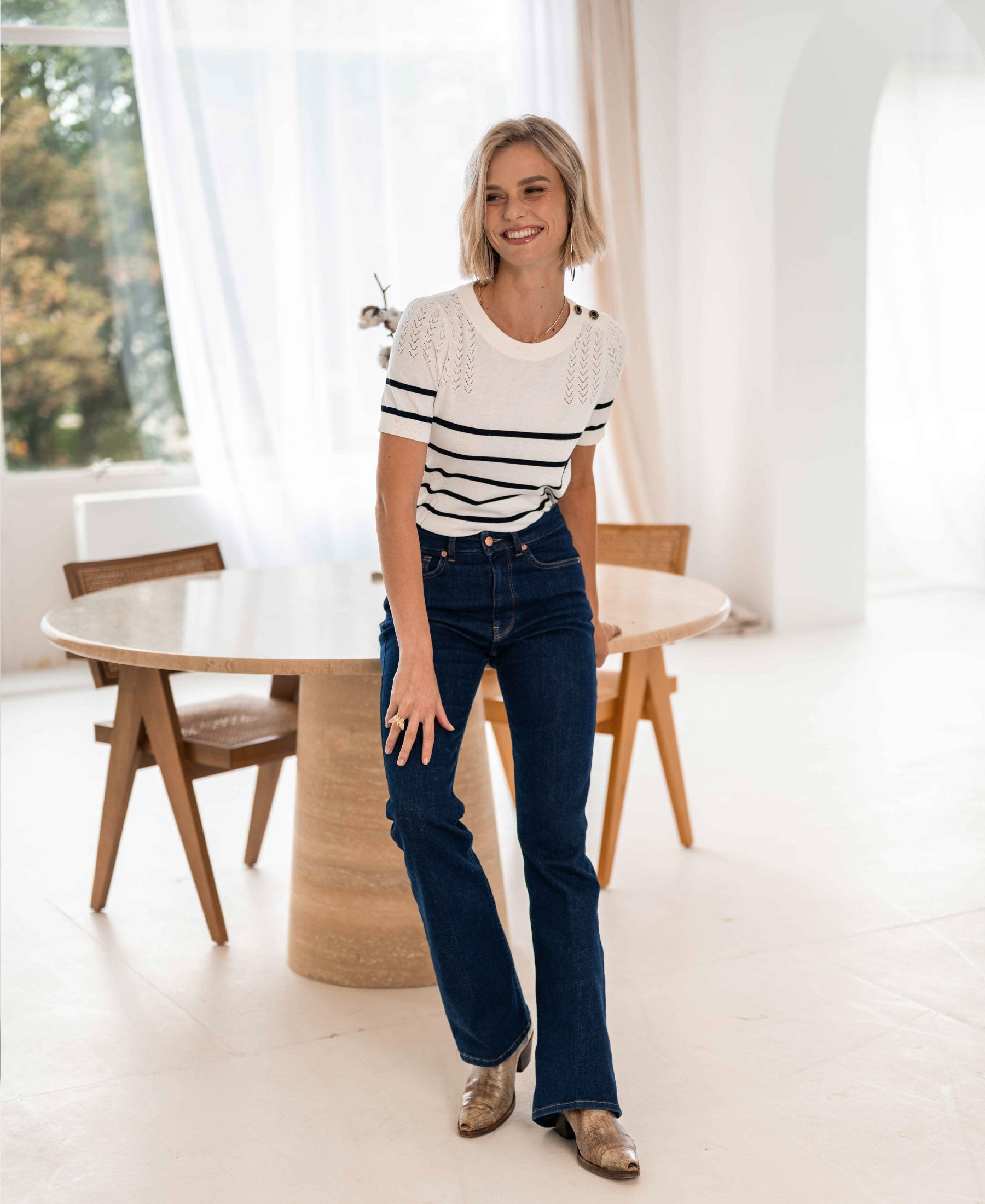 Woman wearing blue rinse-wash flared jeans stands in a modern room.
