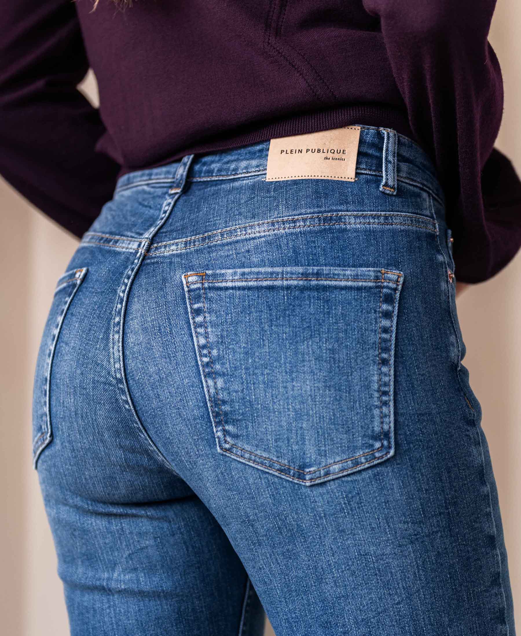 Close-up of a person wearing blue stretch denim flared jeans in stonewash, showing back pocket.