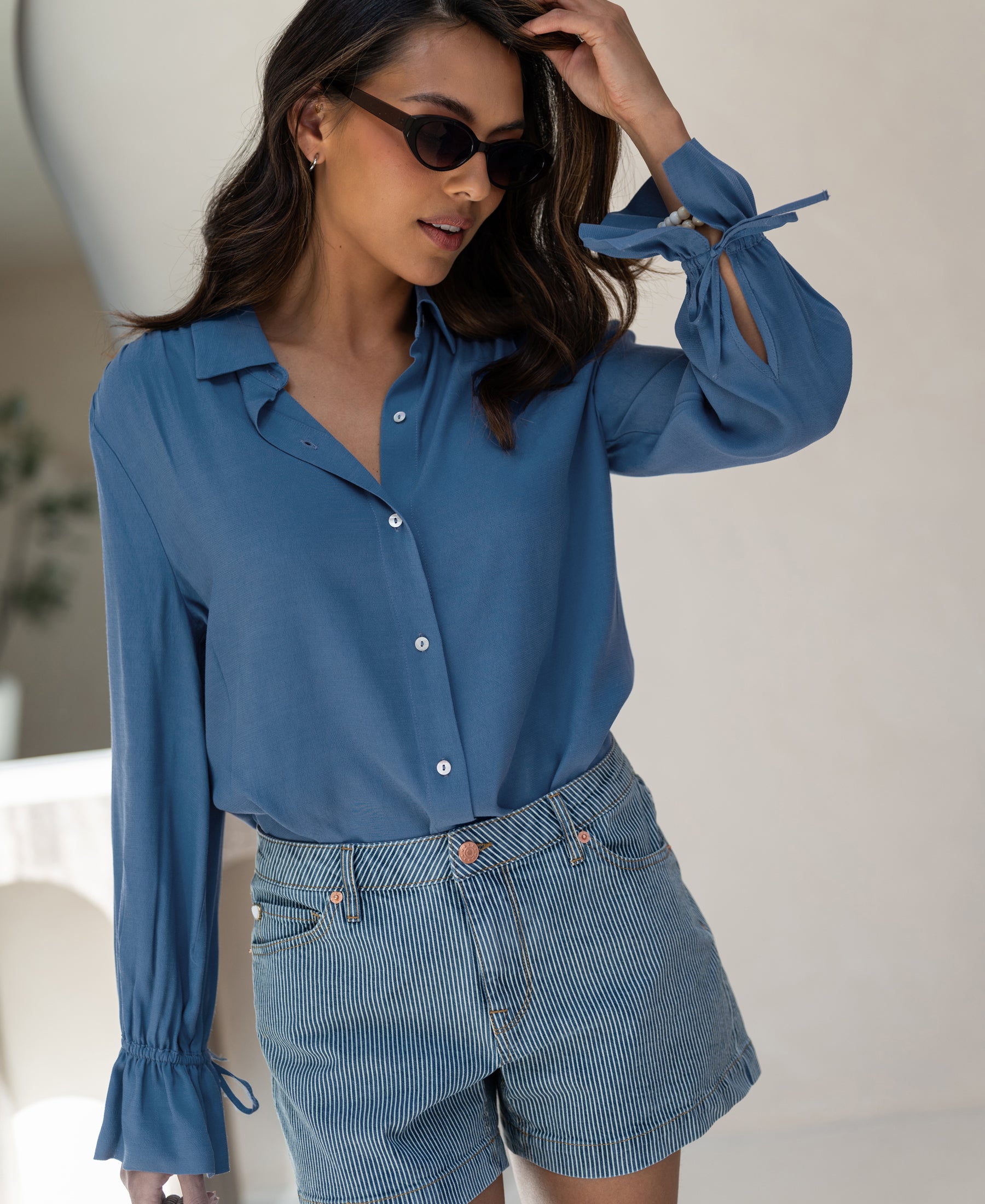 Woman wears a blue PLEIN PUBLIQUE LA TROYES blouse, standing indoors.
