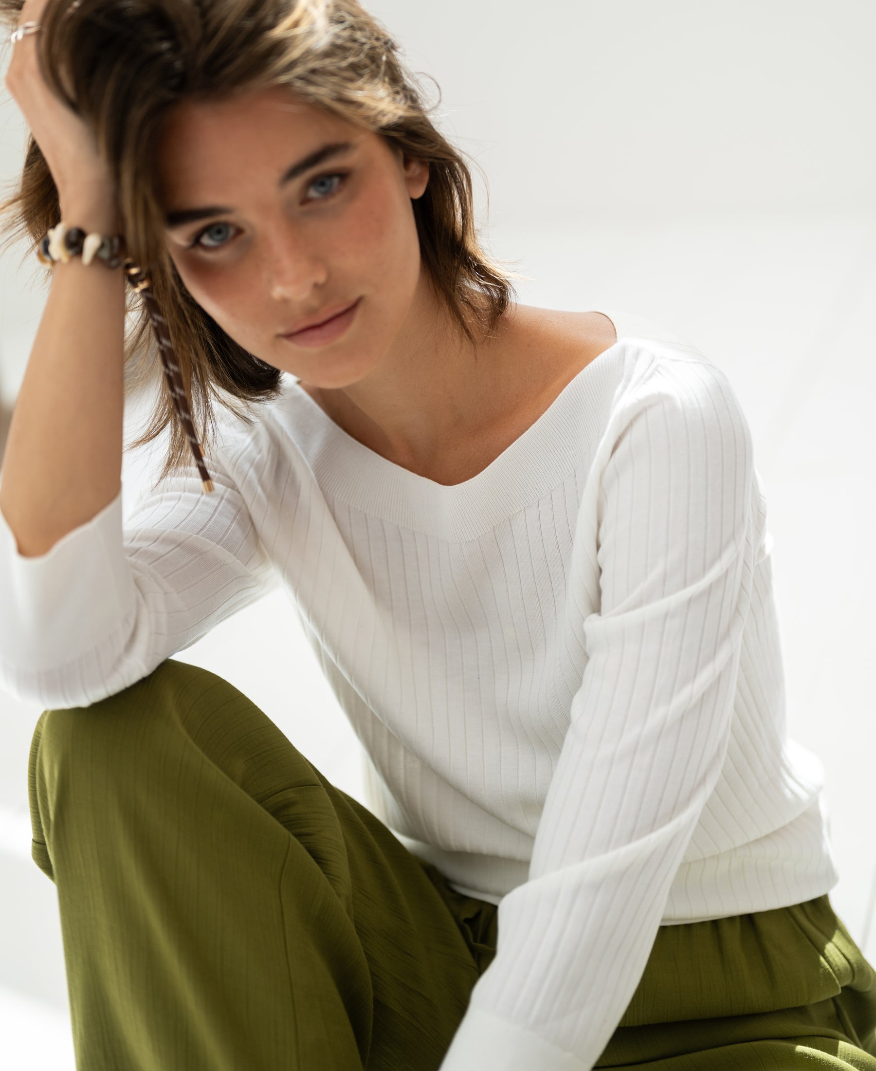 White PLEIN PUBLIQUE Tencel-silk bateau neck sweater LA TULIPE shown worn by a woman sitting in natural light.