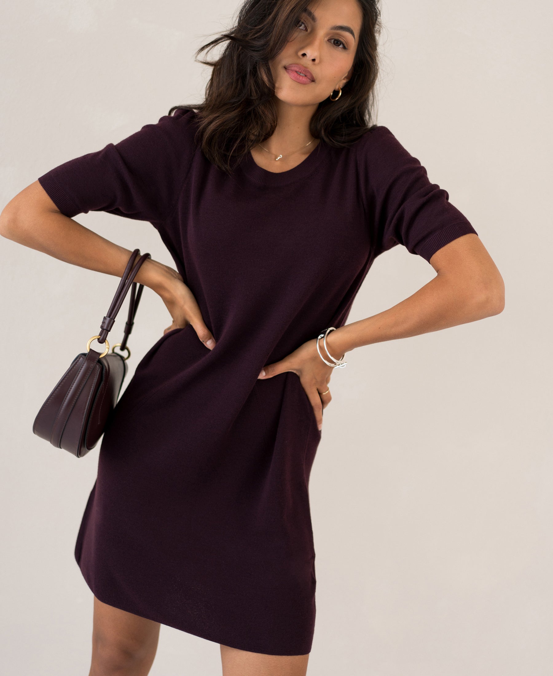 Woman wearing a Plein Publique merino wool dress in aubergine, hands on hips.