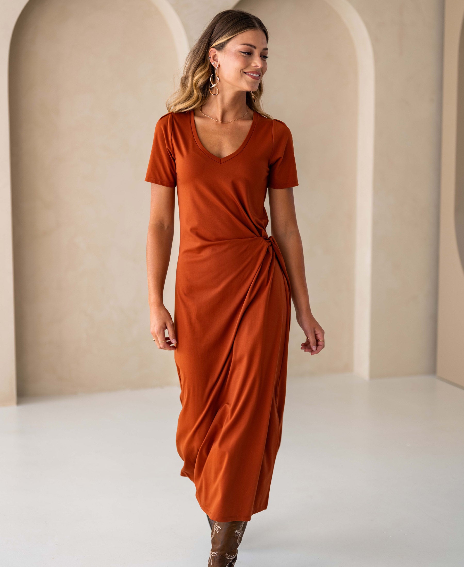 Terra-colored long dress by PLEIN PUBLIQUE displayed in a minimal beige room.