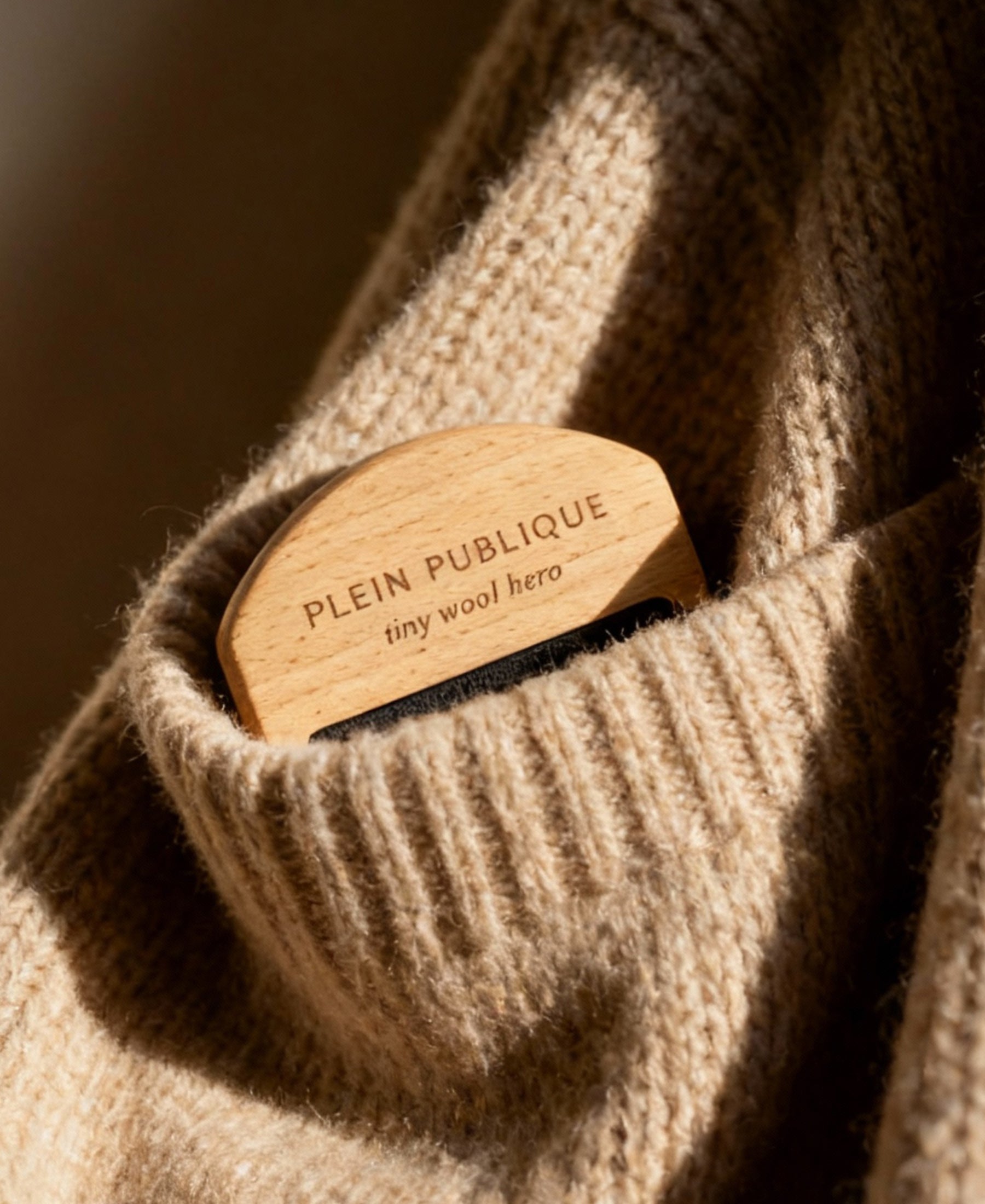 A small wool comb from PLEIN PUBLIQUE shown resting on a beige merino wool sweater.