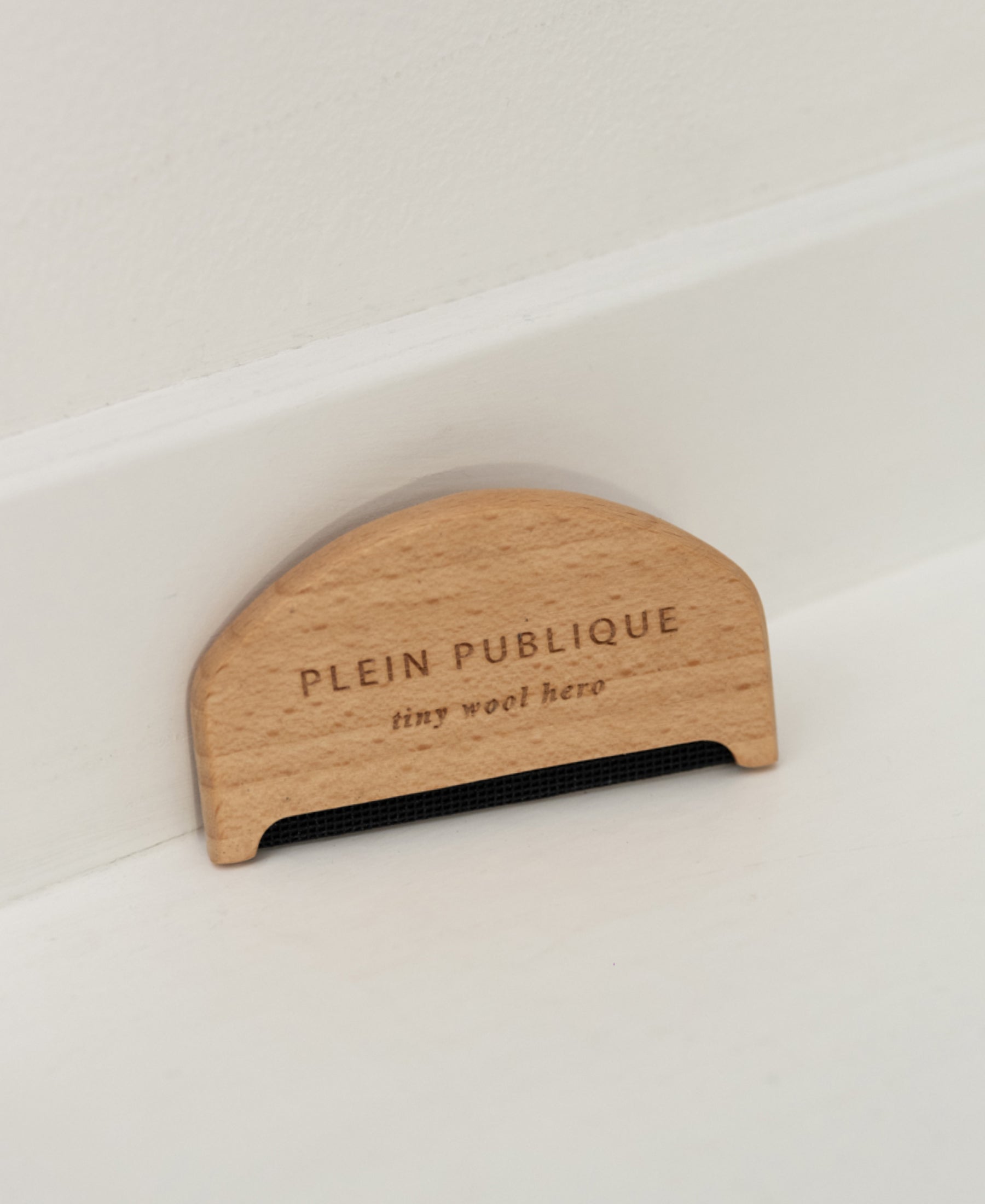 The small wool comb rests against a white wall and baseboard.