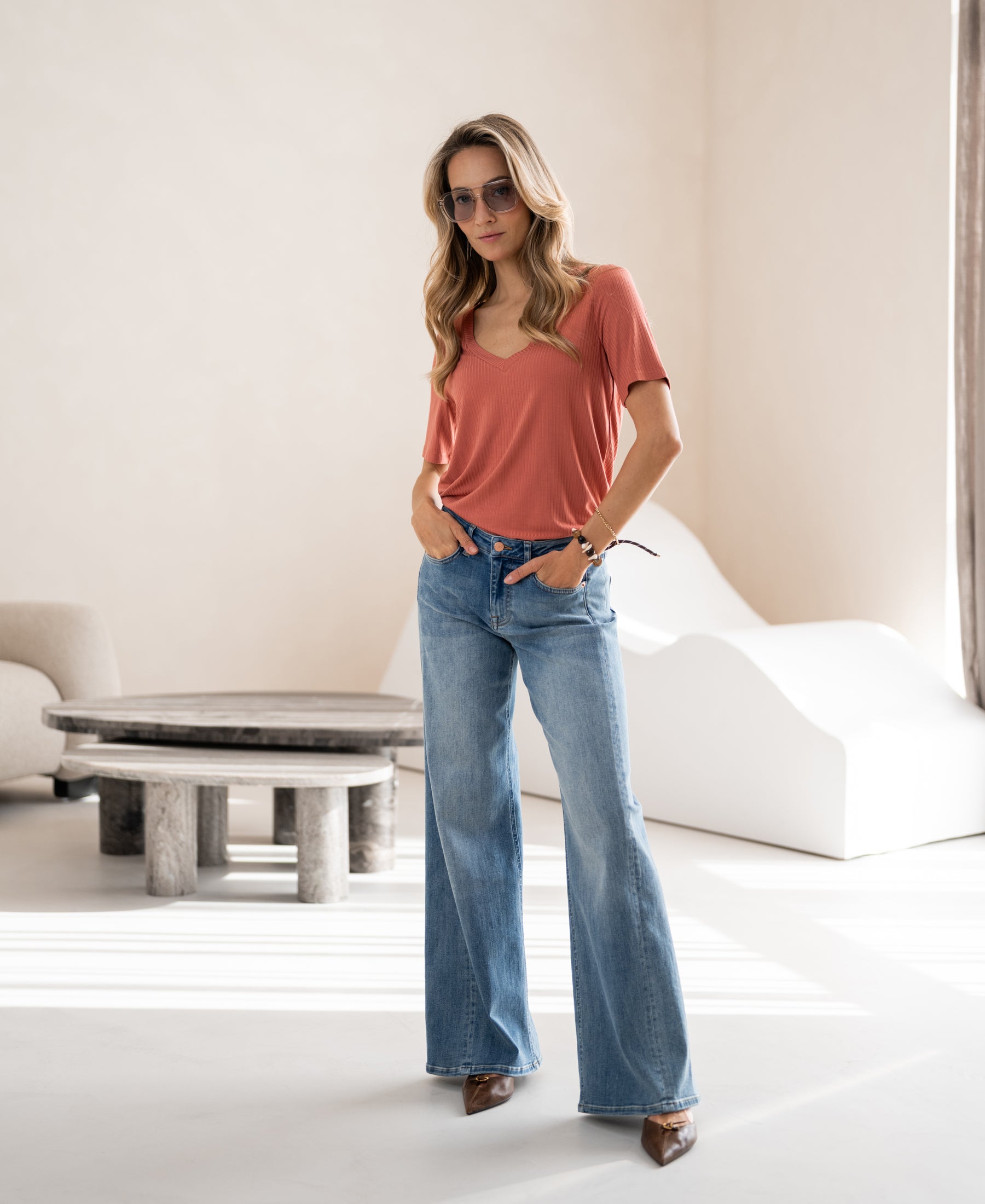 Woman wearing OVERIG’s bamboo T-shirt in bright terra color, standing with hands in pockets.