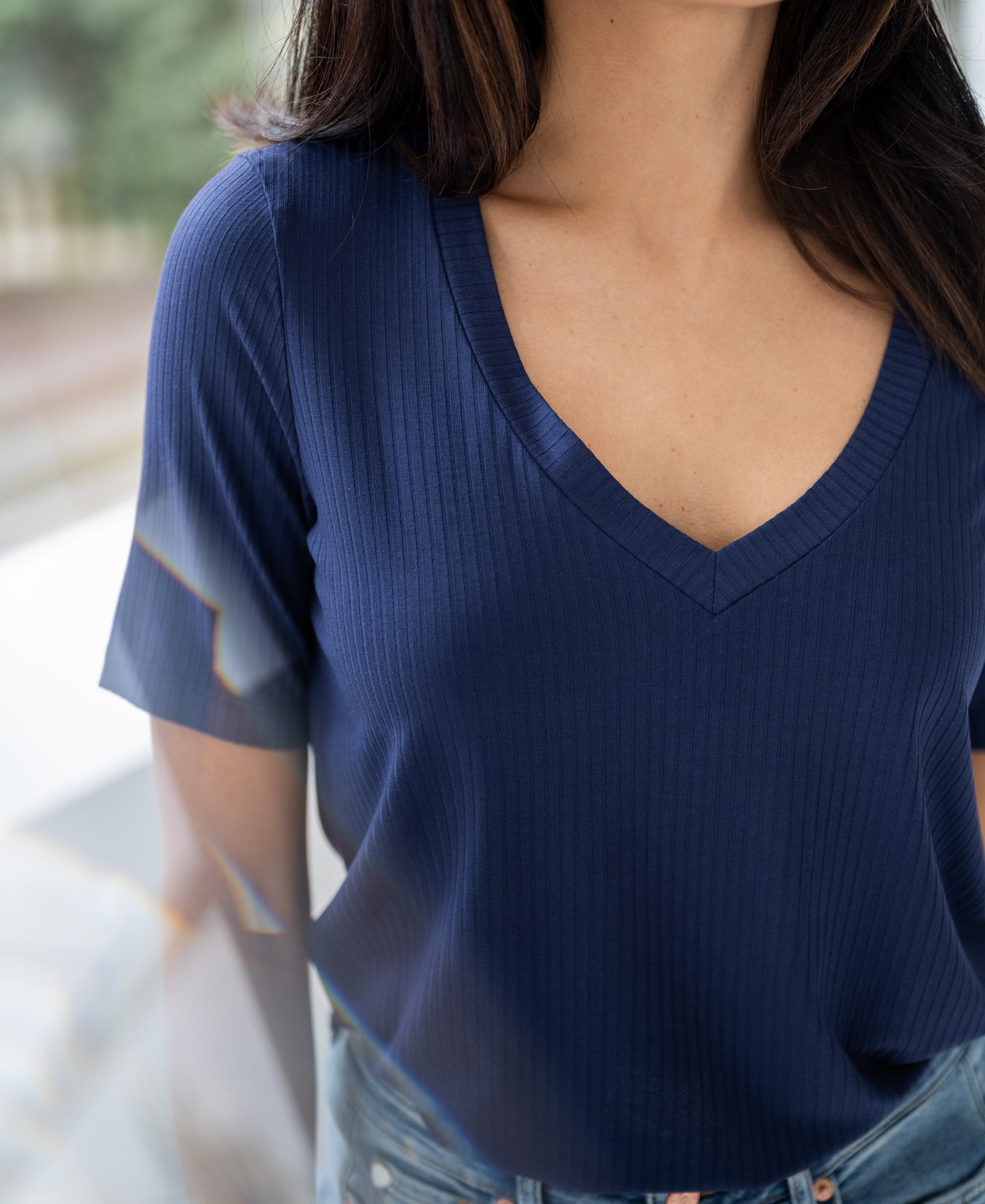 Woman wearing bamboo T-shirt in denim blue (indigo), indoors by window, head partly cropped.