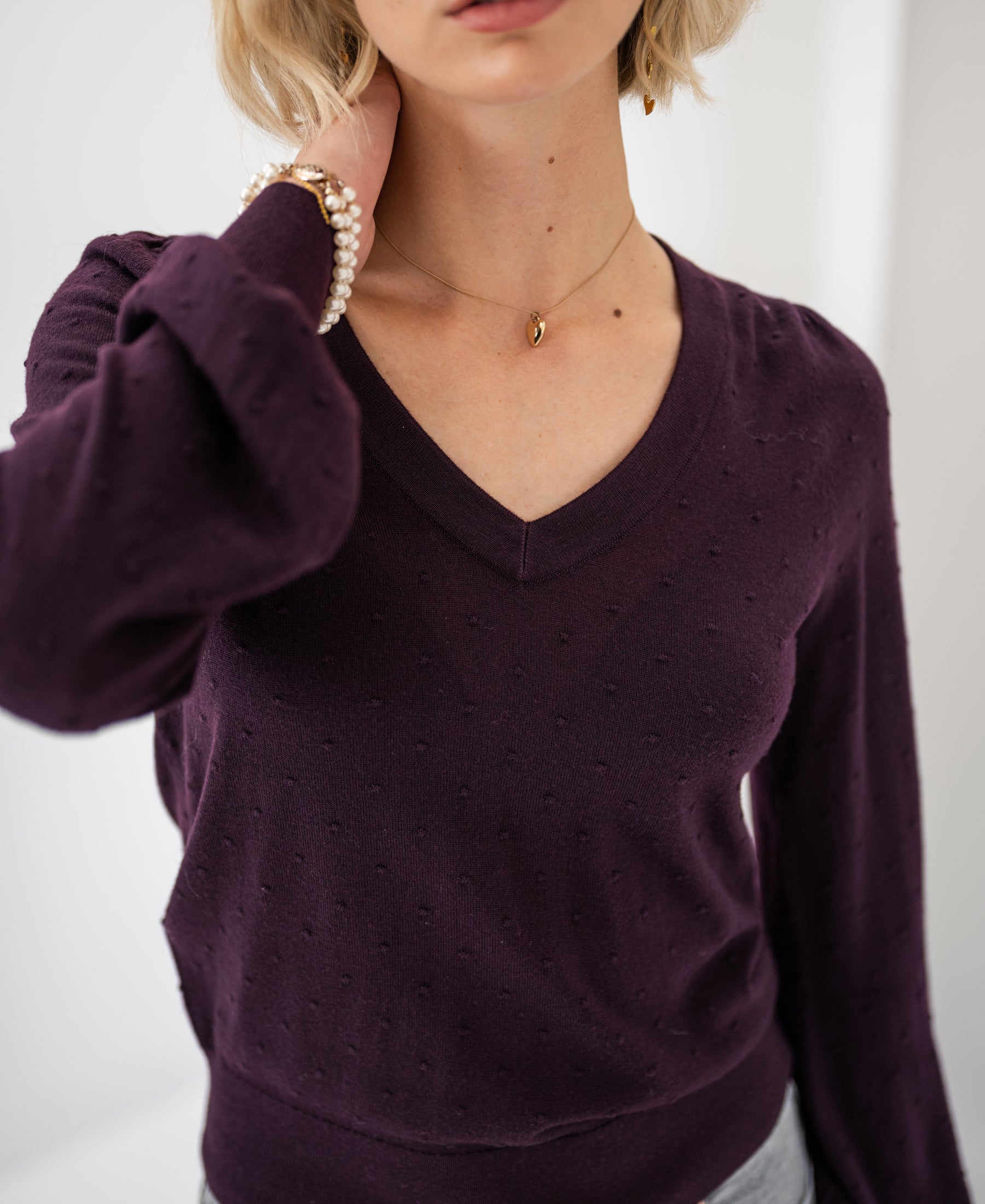 Woman wearing a PLEIN PUBLIQUE Merino wool V-neck sweater in aubergine.