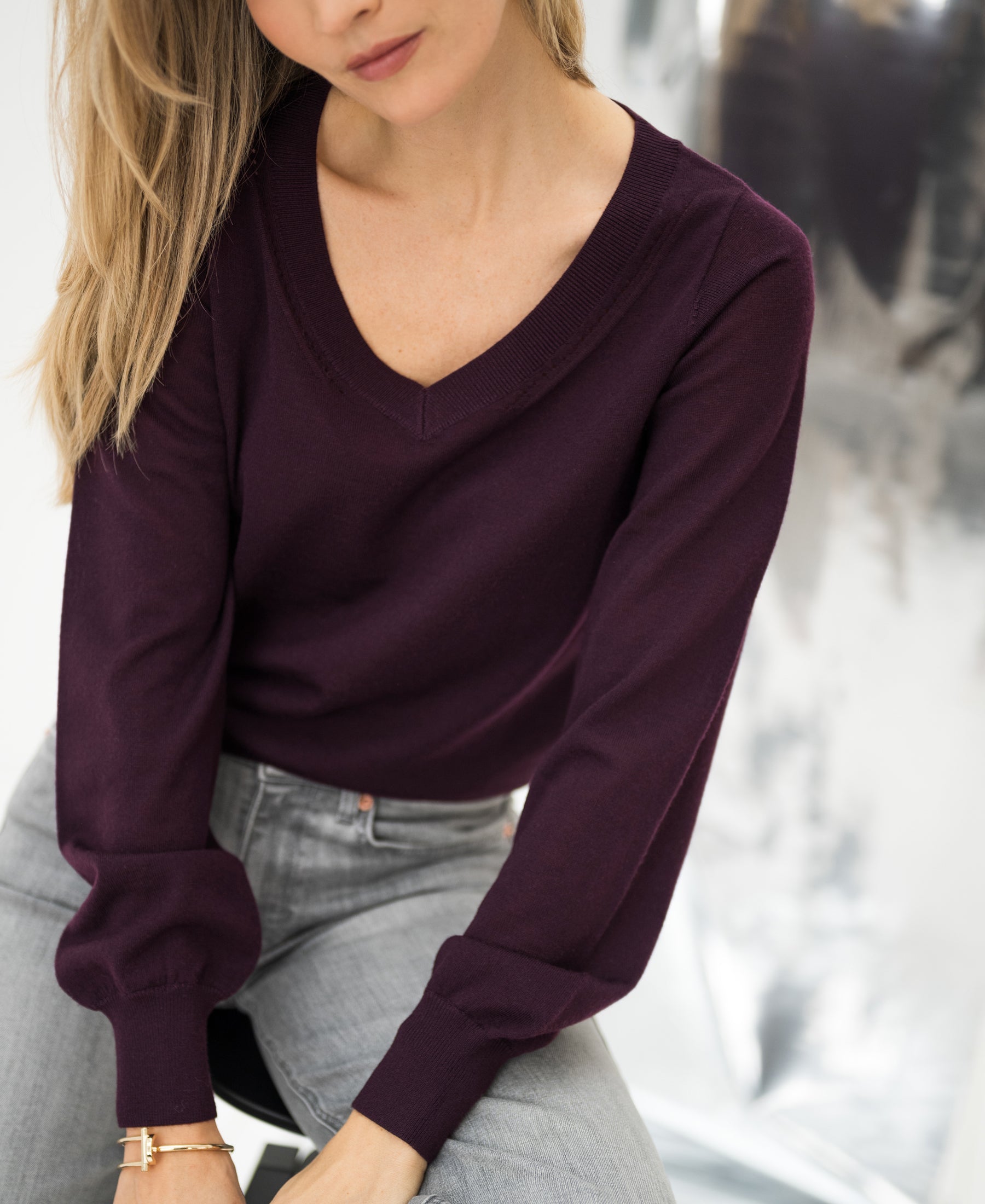 Woman wearing the PLEIN PUBLIQUE Merino V-neck sweater LA VILLE in aubergine, soft background.