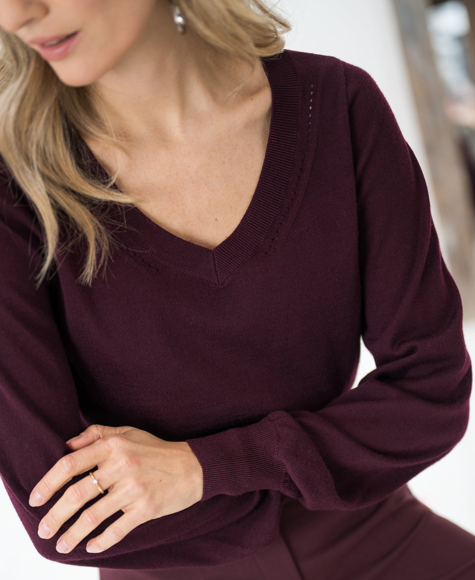 Woman wearing the Merino V-neck sweater LA VILLE in Bordeaux from PLEIN PUBLIQUE, arms crossed.