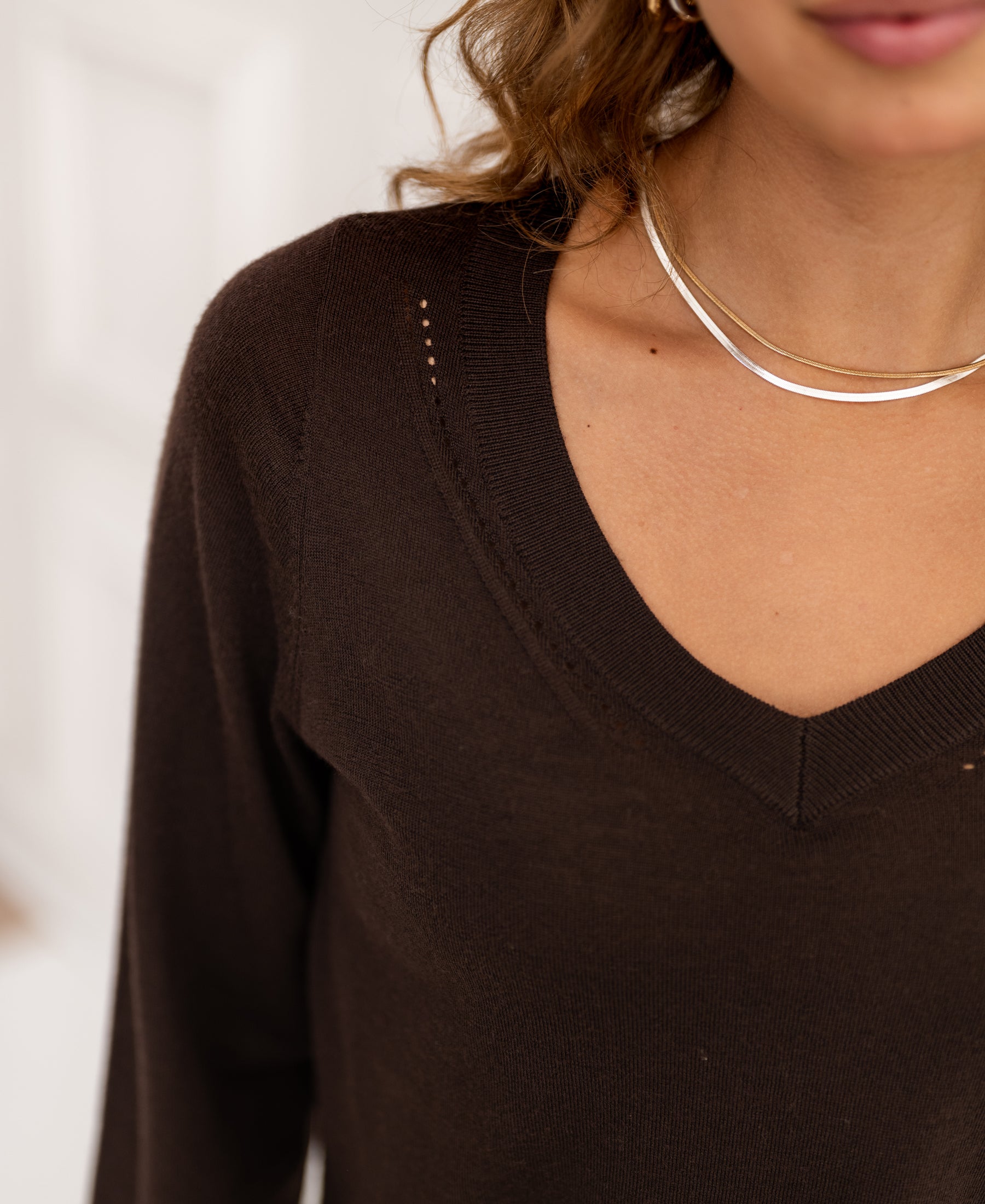 Woman wears the Merino wool V-neck sweater in pure chocolate brown, shown from shoulders up.