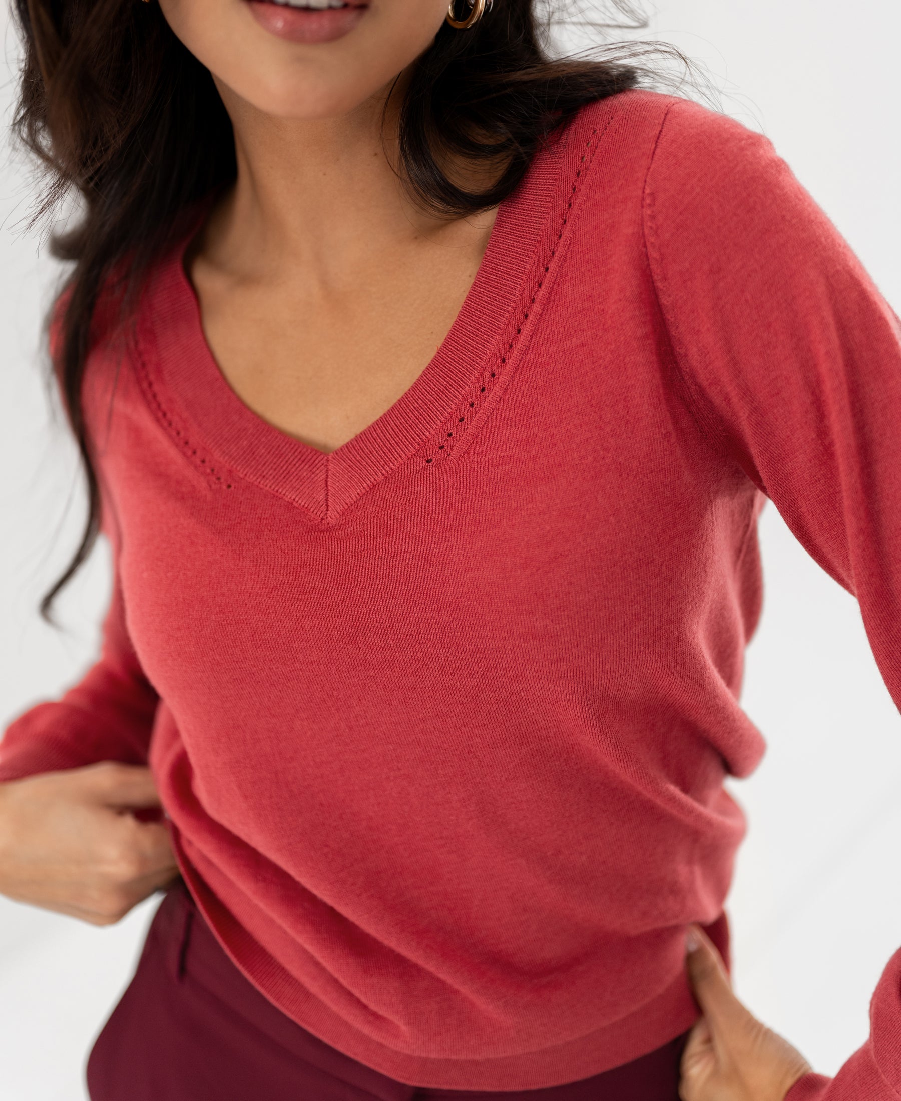 Woman wearing the PLEIN PUBLIQUE Merino wool V-neck sweater in red, hand on hip against a light background.