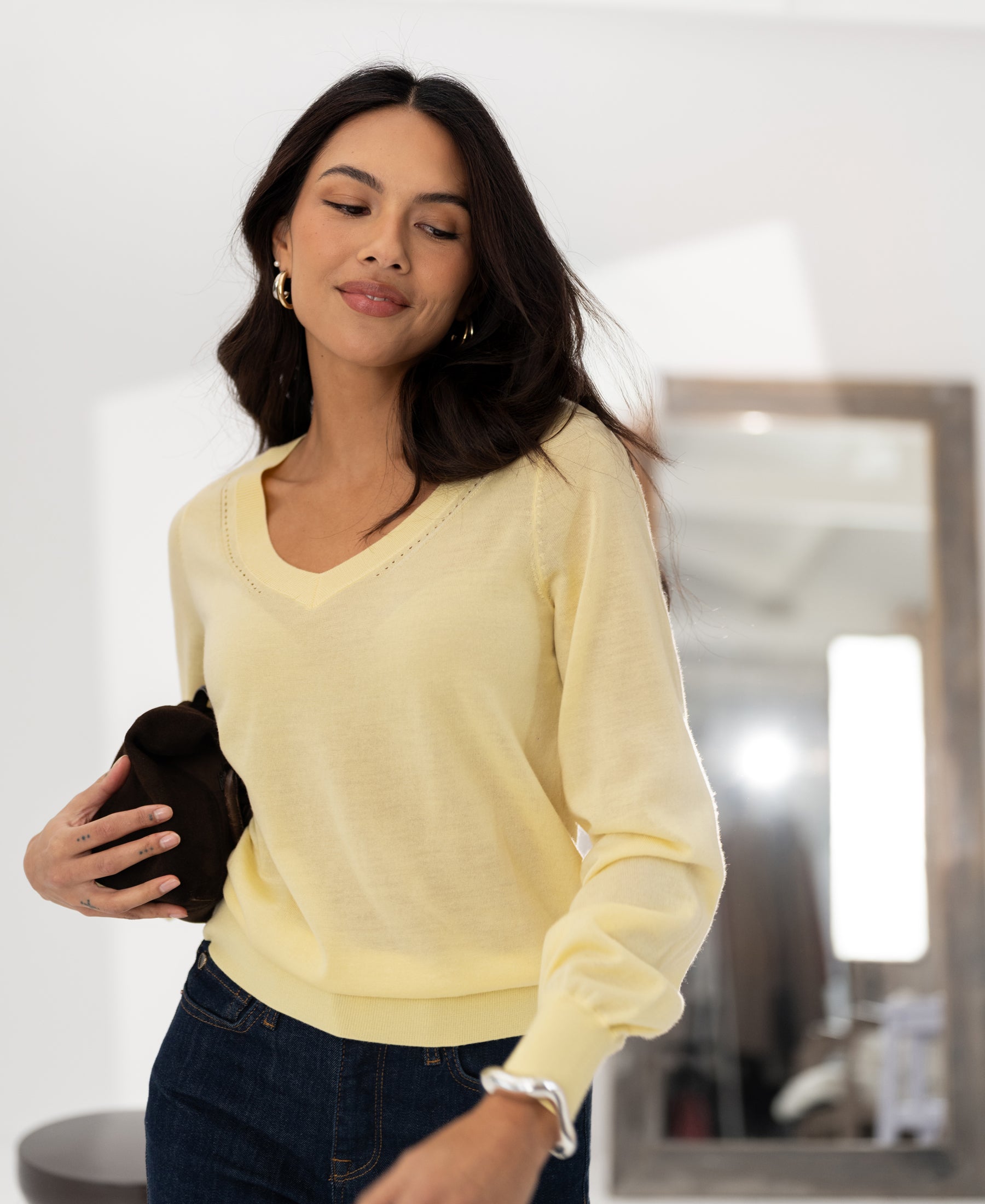 Woman in the LA VILLE Soft Yellow Merino V-neck sweater by PLEIN PUBLIQUE, looking to the side by a mirror.
