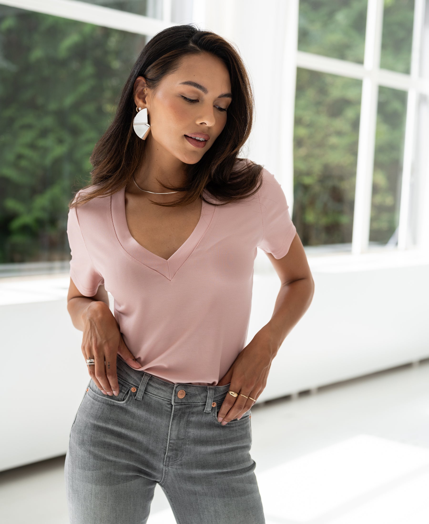 Dusty pink lyocell T-shirt displayed on model in front of windows with greenery.