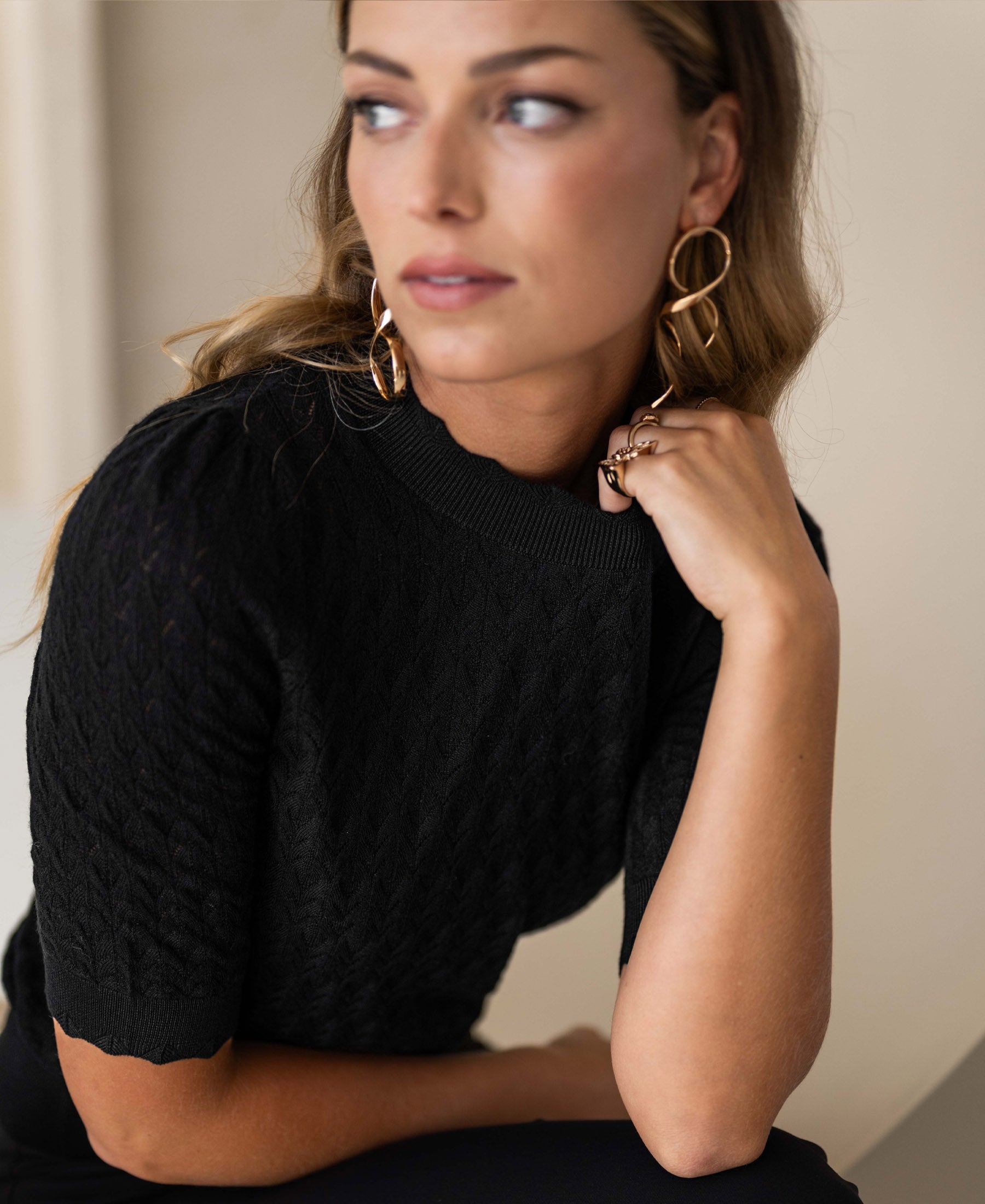 Woman wearing a black merino wool sweater, gazing sideways with hand near face.