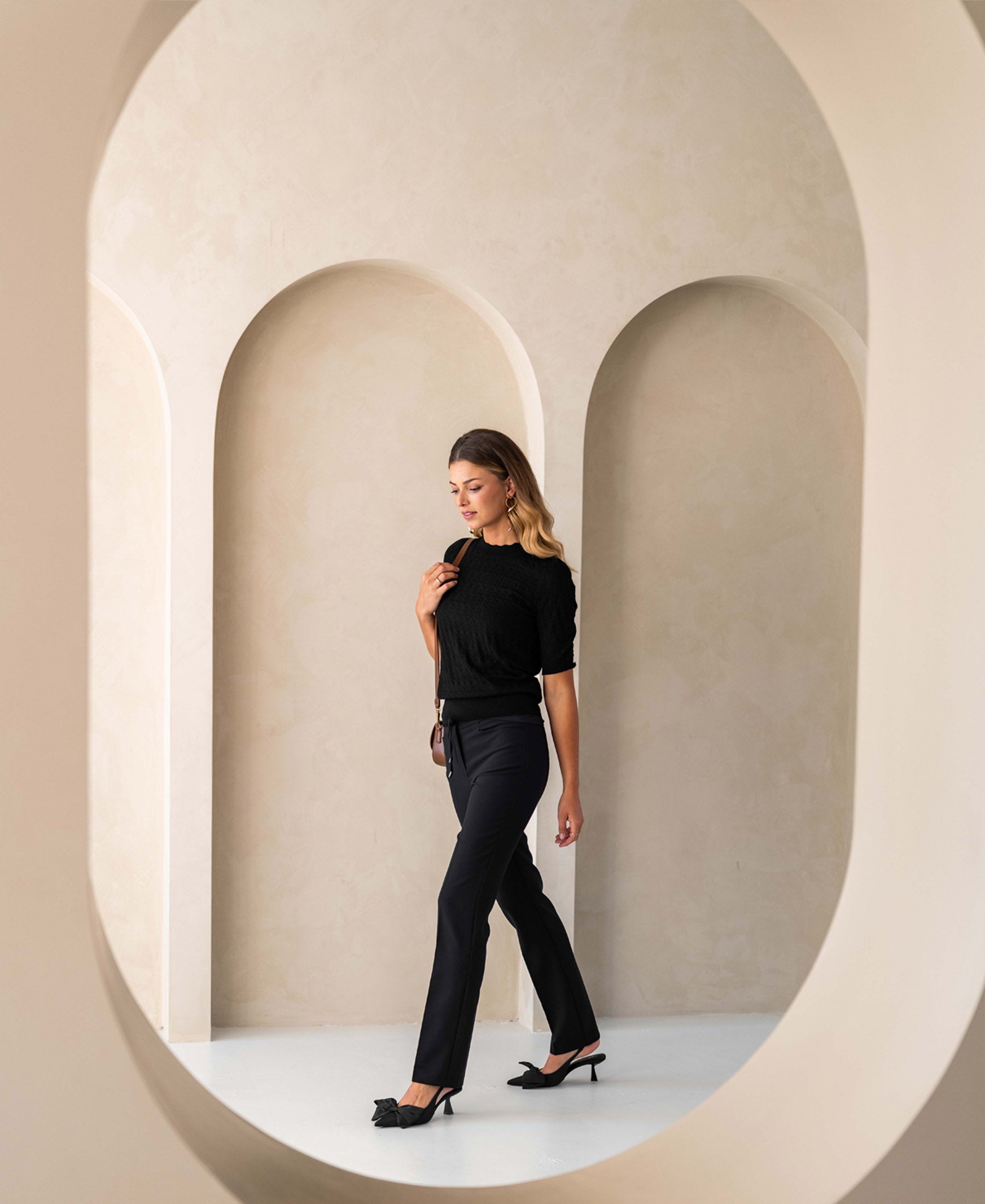 Black merino wool sweater for women, shown in a modern neutral-tone archway interior.