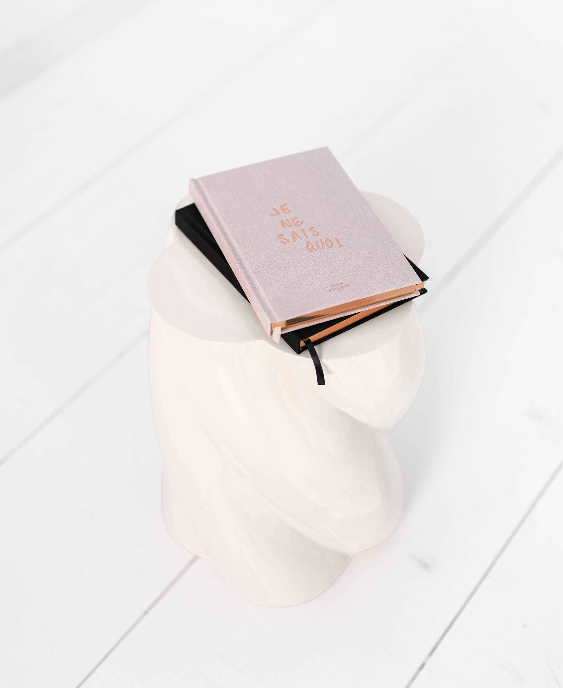 A natural-colored notebook with "I Don't Know What" on the cover displayed on a white sculpted stool.