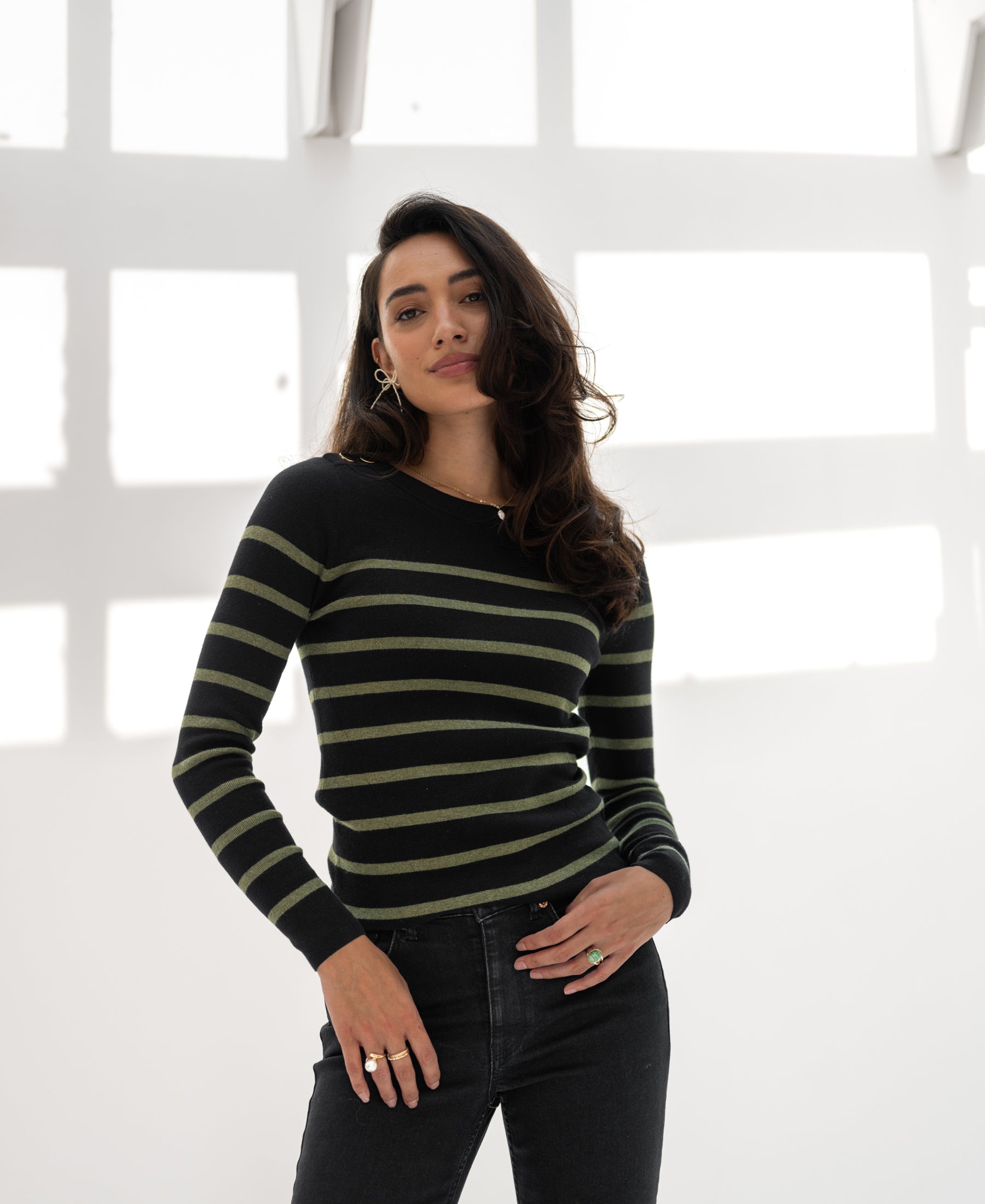 L'ELISA Black-Army Green sweater by PLEIN PUBLIQUE shown in sunlight against white walls and window shadows.