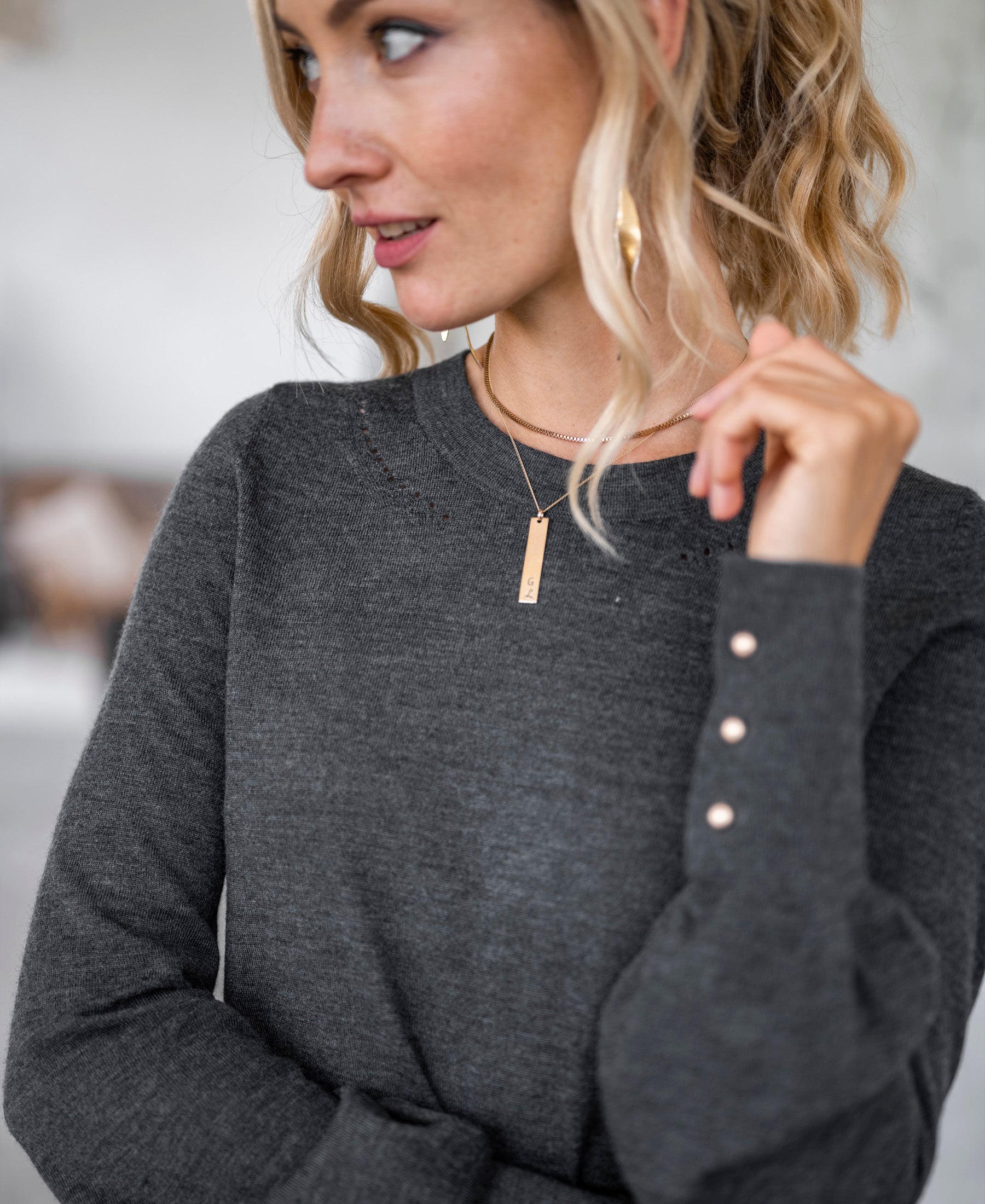Woman wearing the LA MARIS Anthracite – Gold Merino wool sweater from PLEIN PUBLIQUE, looking to the side.