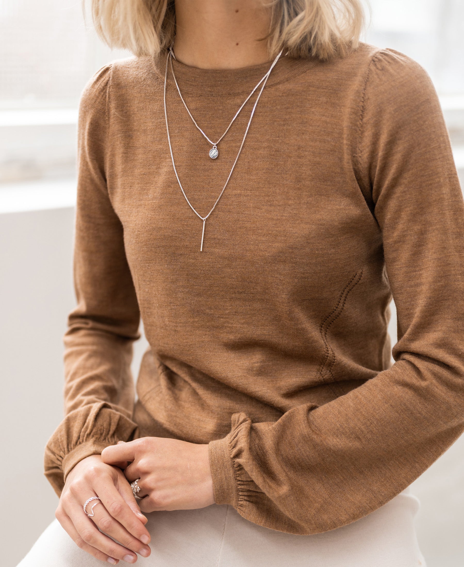 Woman wearing a Plein Publique merino wool La Coeur Chai Tea sweater, hands on lap.