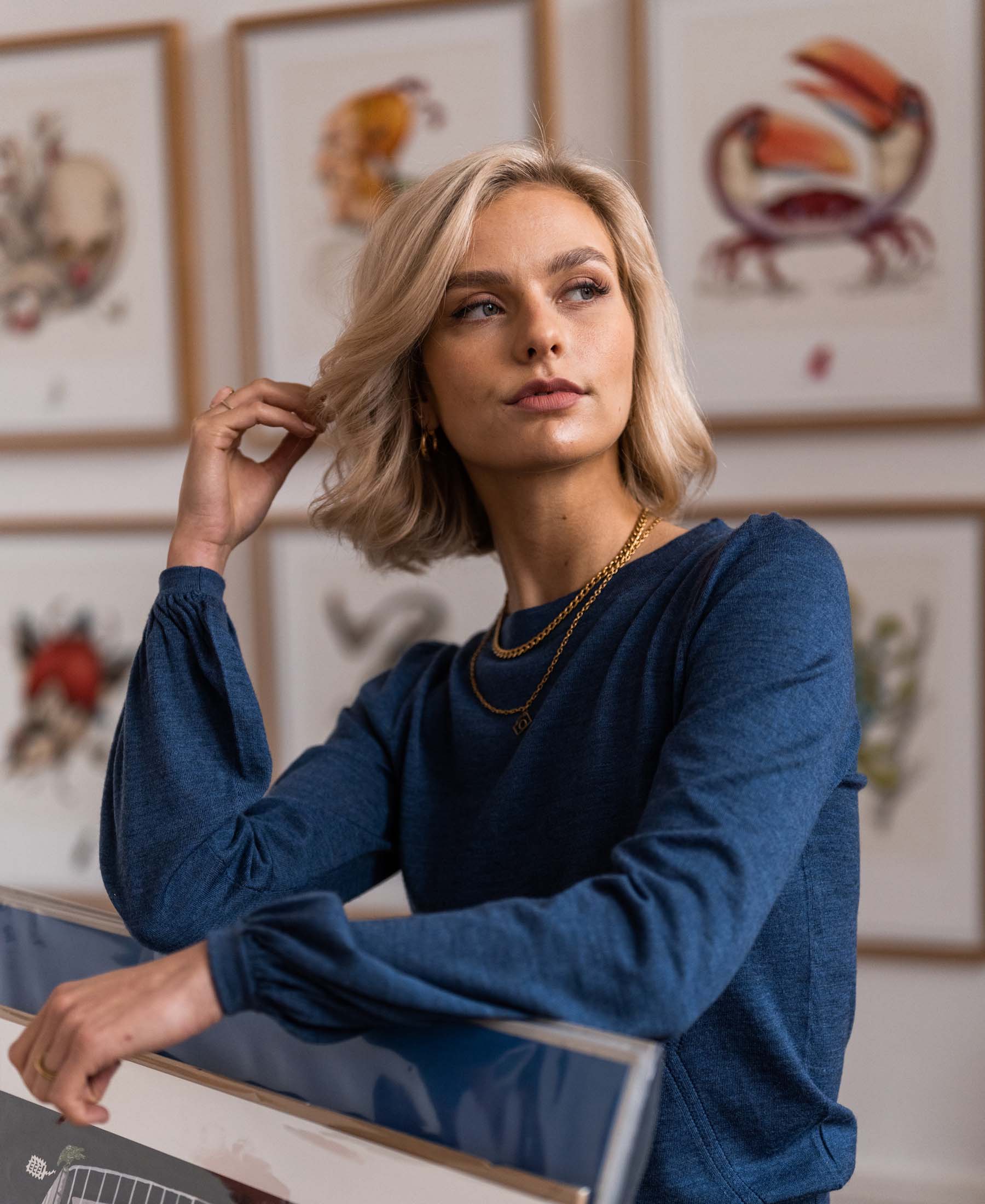 Woman wears PLEIN PUBLIQUE LA COEUR indigo blue merino sweater, posing indoors.