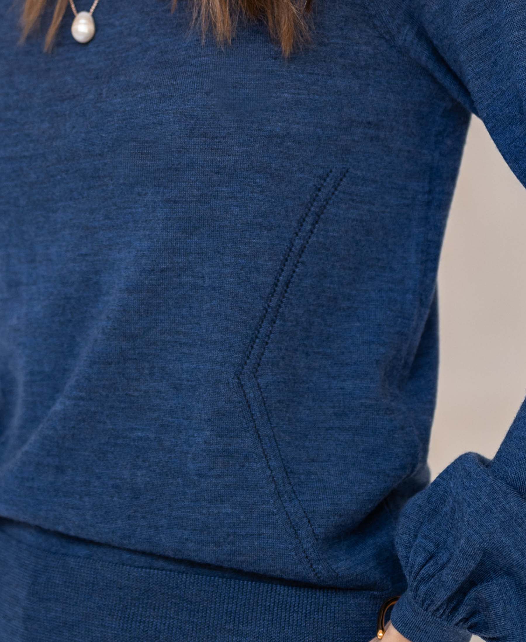Close-up of indigo blue merino wool sweater with balloon sleeves, side pocket, and pearl accents.