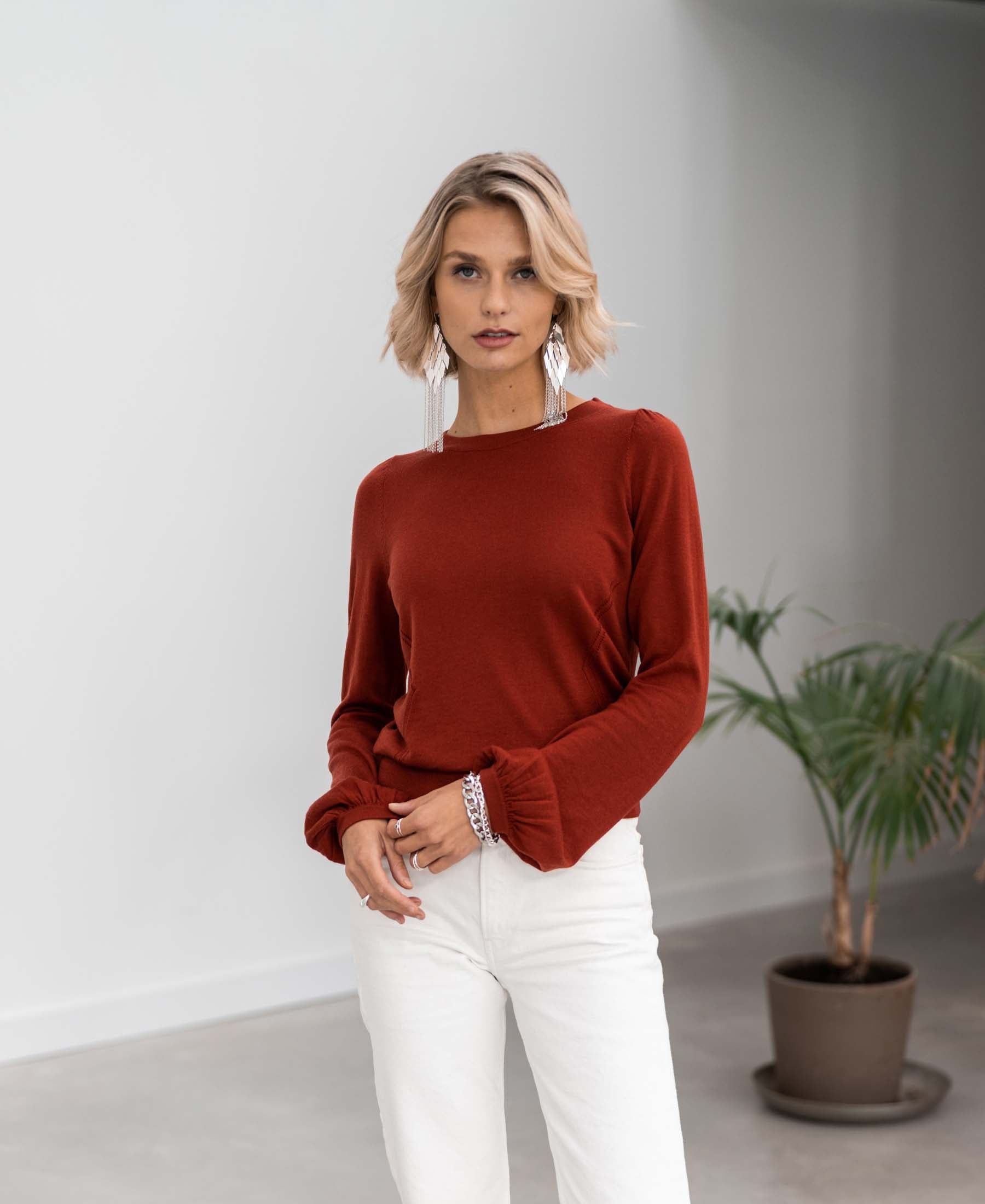 Woman wearing a rosewood Merino wool sweater indoors by a plant.
