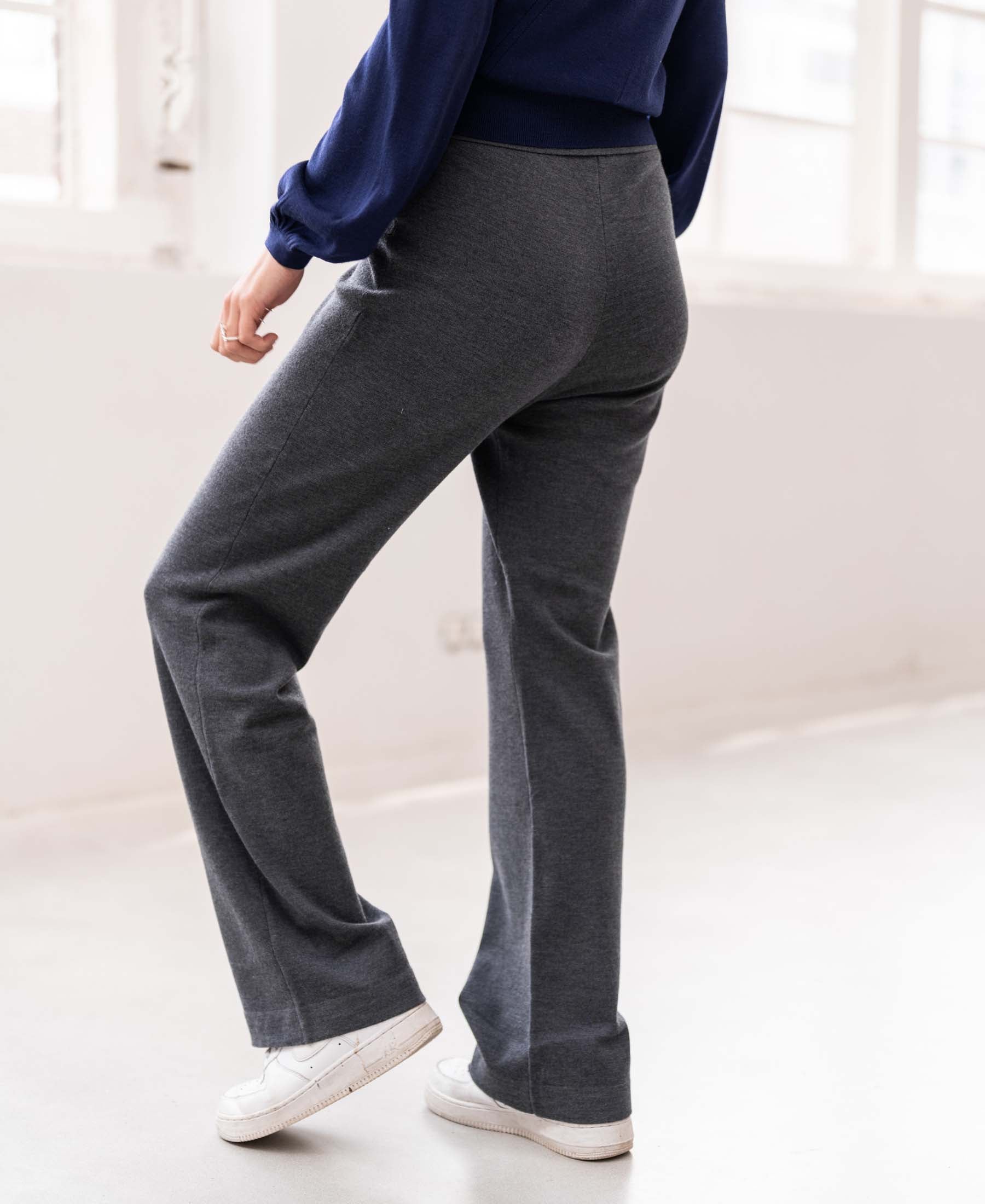 Person wearing anthracite knit trousers in a minimal room.