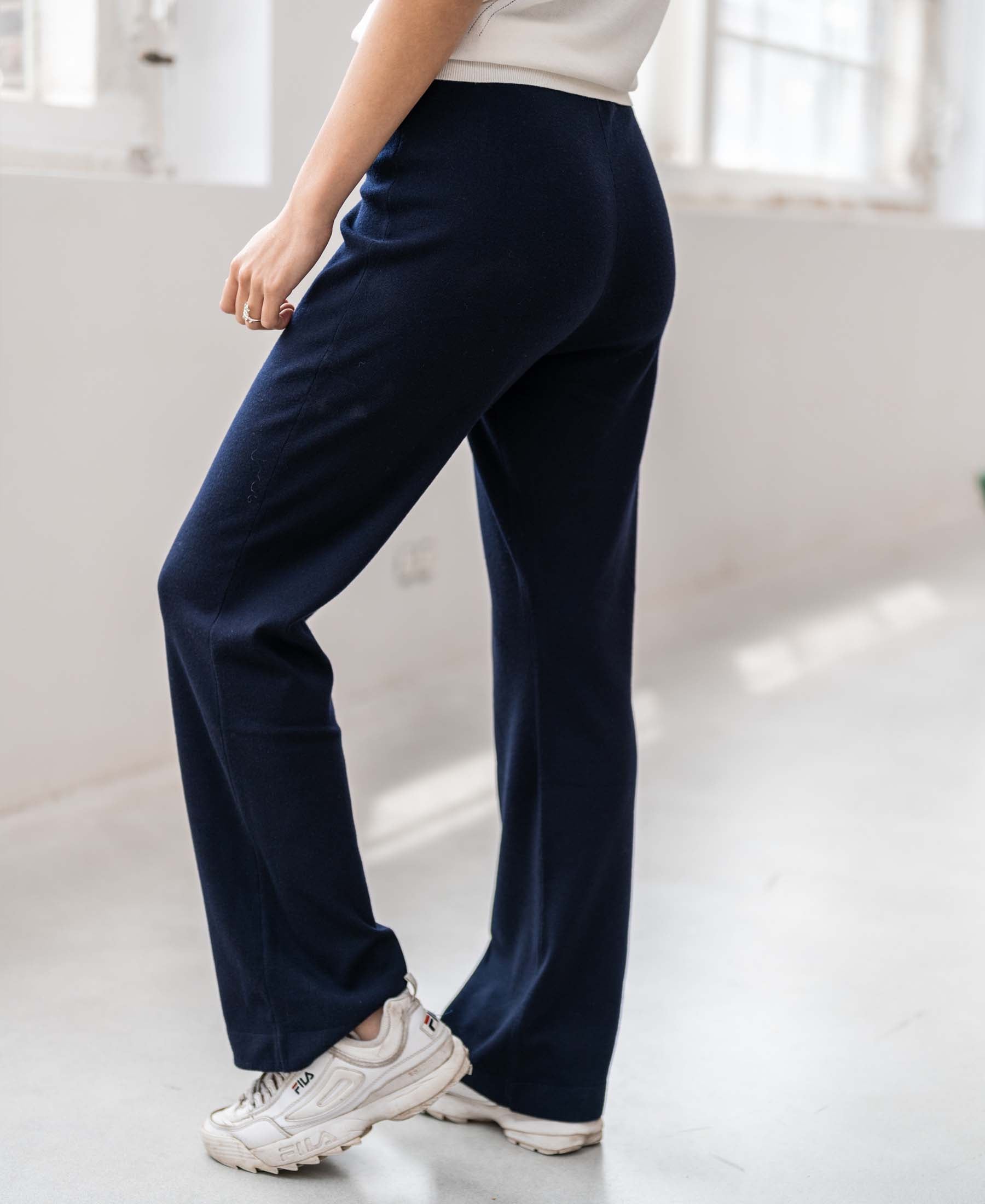 Person wearing dark blue PLEIN PUBLIQUE knitted pants indoors by windows.