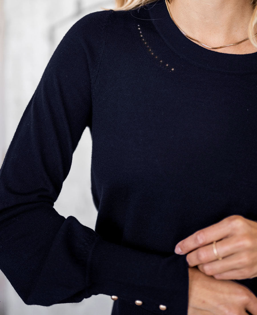 Woman wears PLEIN PUBLIQUE Merino wool sweater LA MARIS in dark blue-gold with gold sleeve buttons.