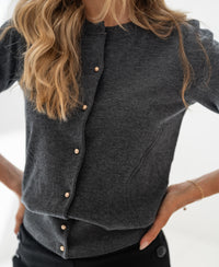 Woman wears PLEIN PUBLIQUE ADELINE cardigan in dark grey with pearl buttons.