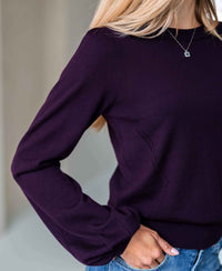 Woman wearing PLEIN PUBLIQUE Merino wool sweater in aubergine, shown from shoulders down.