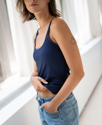 Woman wearing a luxurious navy camisole top made of soft fabric, shown from the front. Sun tattoo visible on her arm.