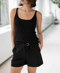 Woman wears Luxe Cami top LE BASTILLE Black by PLEIN PUBLIQUE indoors, hands in pockets.