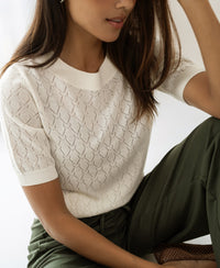 Woman wearing the LE BATTANT Ivory sweater by PLEIN PUBLIQUE, seated indoors.