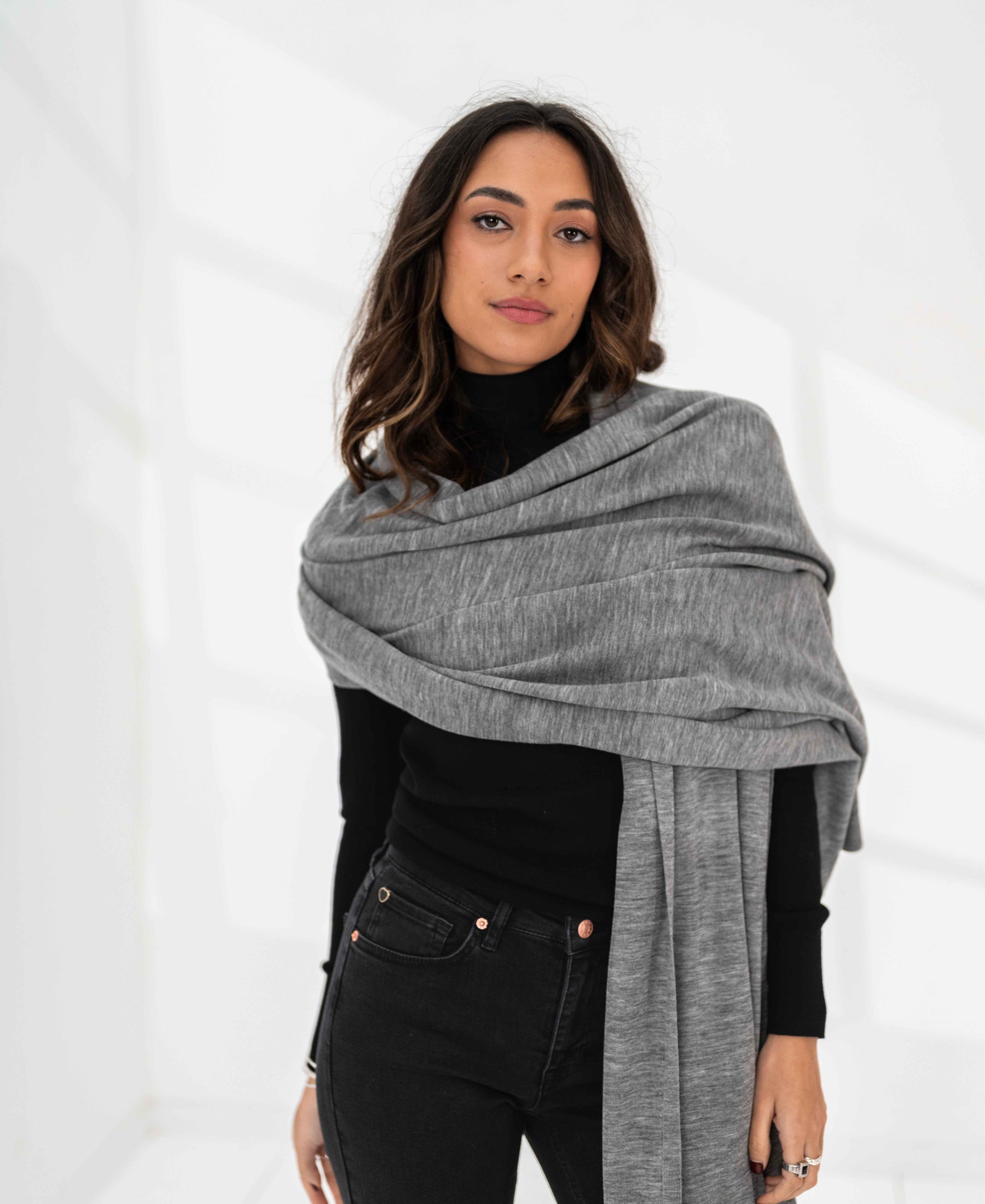 Woman wearing a grey melange PLEIN PUBLIQUE Merino wool maxi scarf looks at the camera.