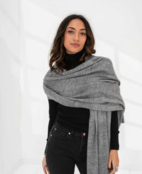 Woman wearing a grey melange PLEIN PUBLIQUE Merino wool maxi scarf looks at the camera.