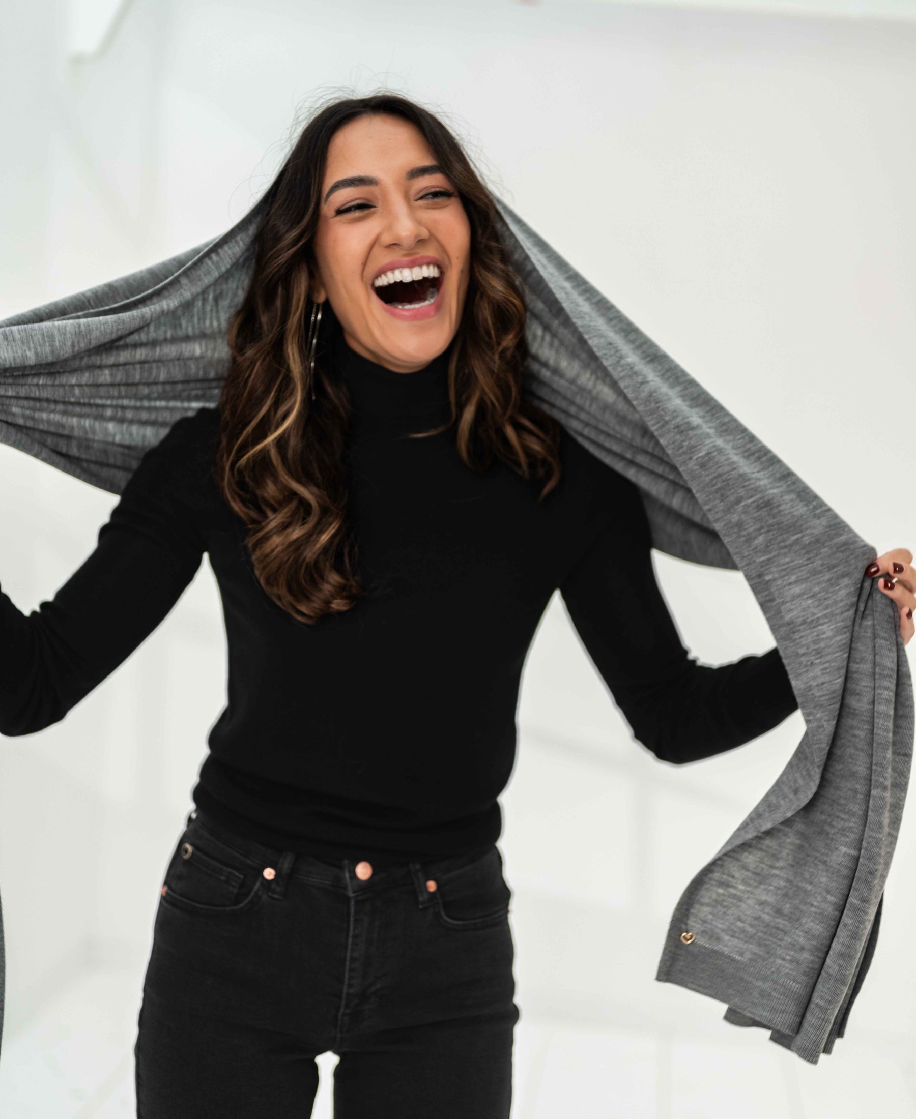 Grey melange Merino wool maxi scarf by PLEIN PUBLIQUE, held by a smiling woman.