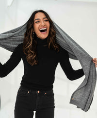 Grey melange Merino wool maxi scarf by PLEIN PUBLIQUE, held by a smiling woman.